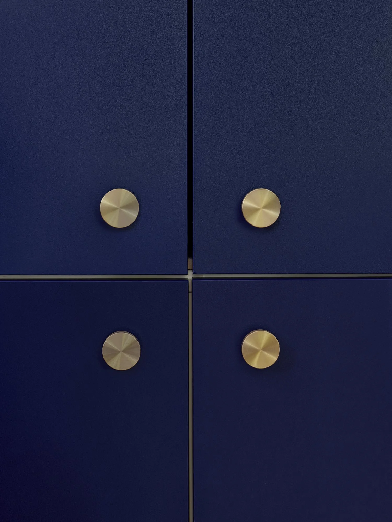 Close-up of four navy blue cabinets with round brass knobs, arranged in a 2x2 grid.