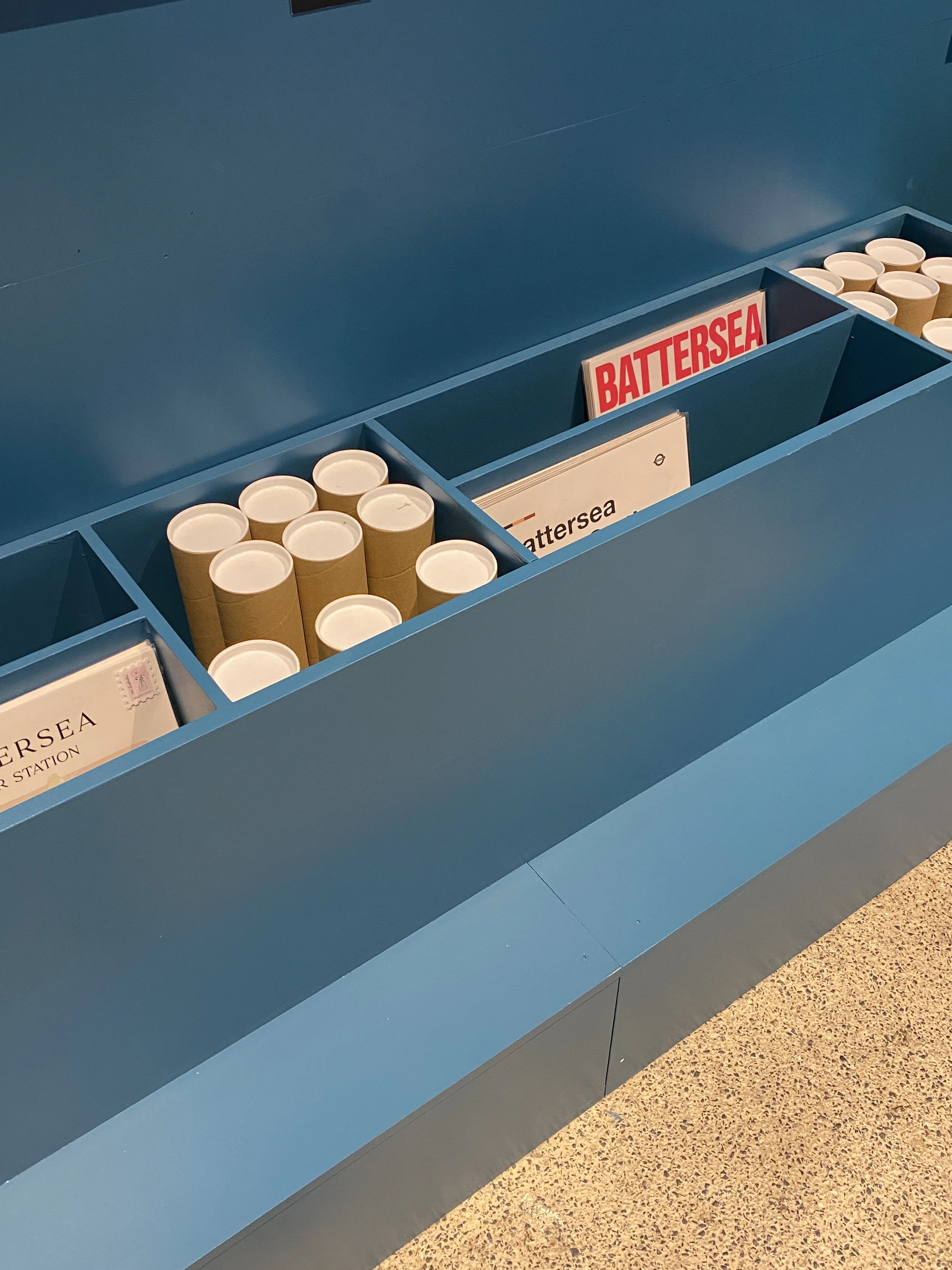 A blue souvenir stand with stacks of empty paper cups and signs labeled 'Battersea'.