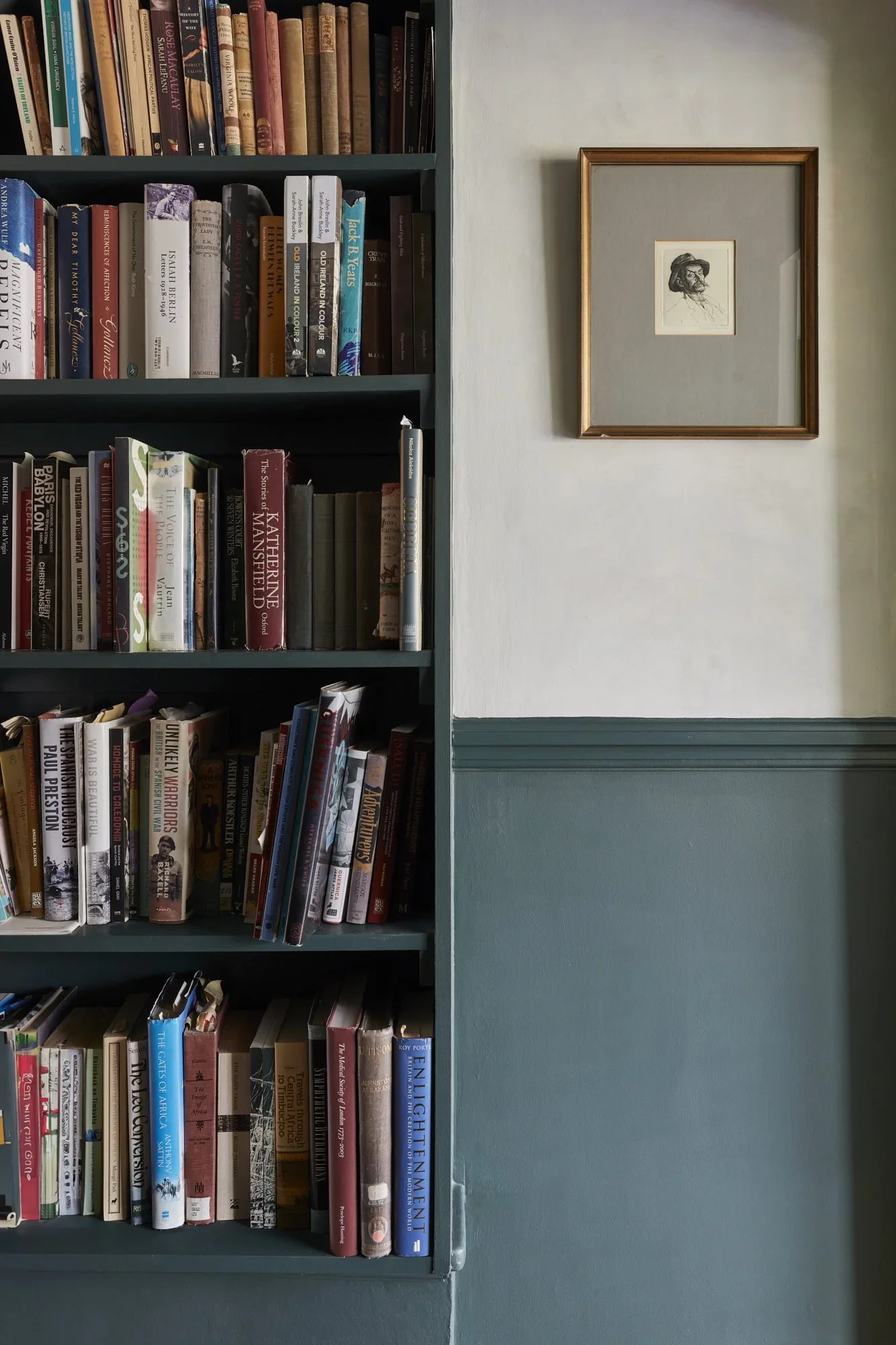 Bookshelf filled with books on the left, with a framed sketch of a person hanging on the wall to the right of the bookshelf.