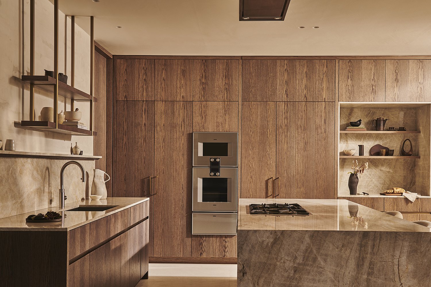 Modern kitchen with wooden cabinets, marble countertop, and open shelving displaying decorative items and dishes.
