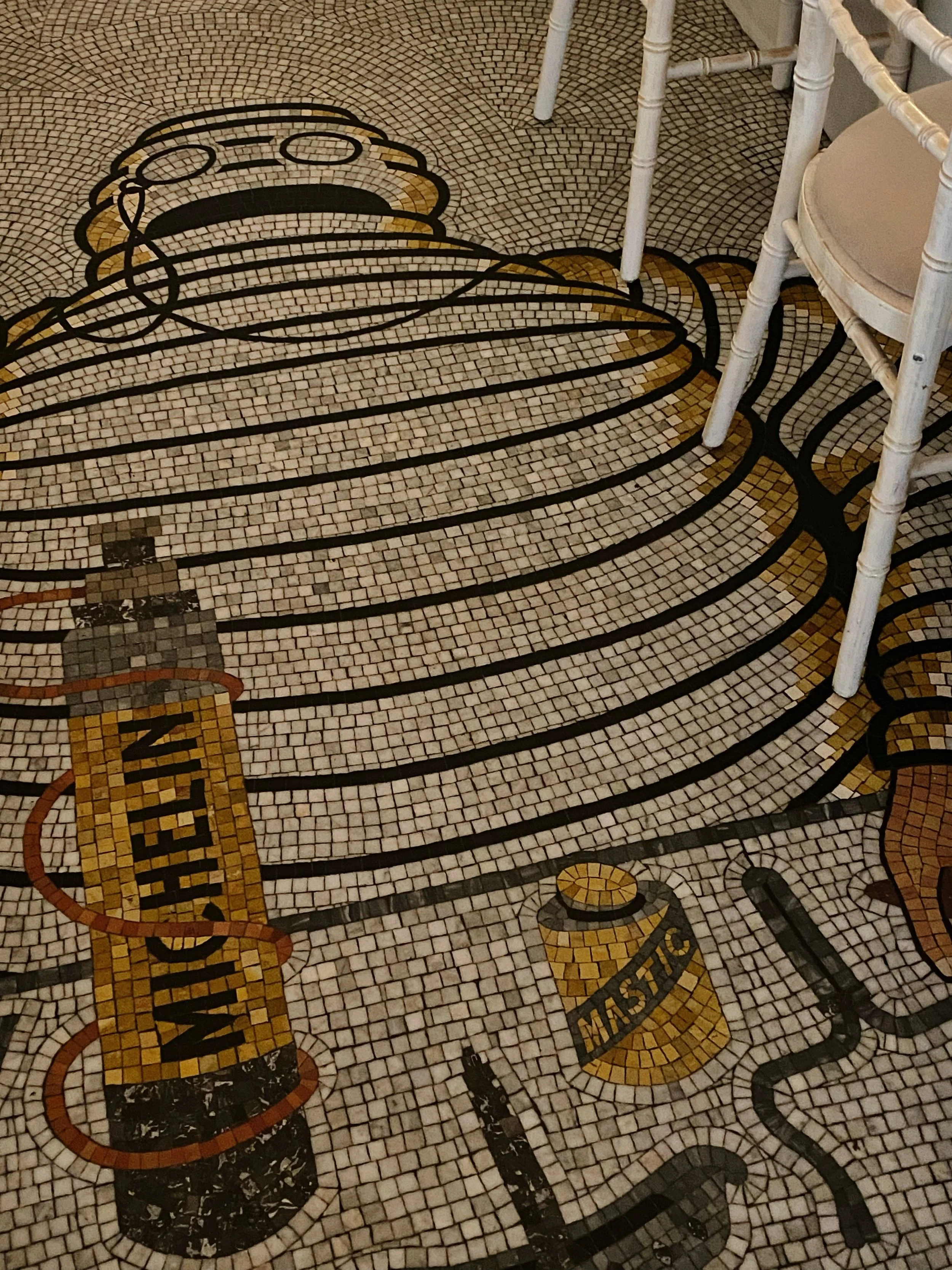 Decorative mosaic floor with outlines of a food tray, a salt shaker labeled 'Salt', and a pepper shaker labeled 'Pepper,' with part of a white chair and table visible.