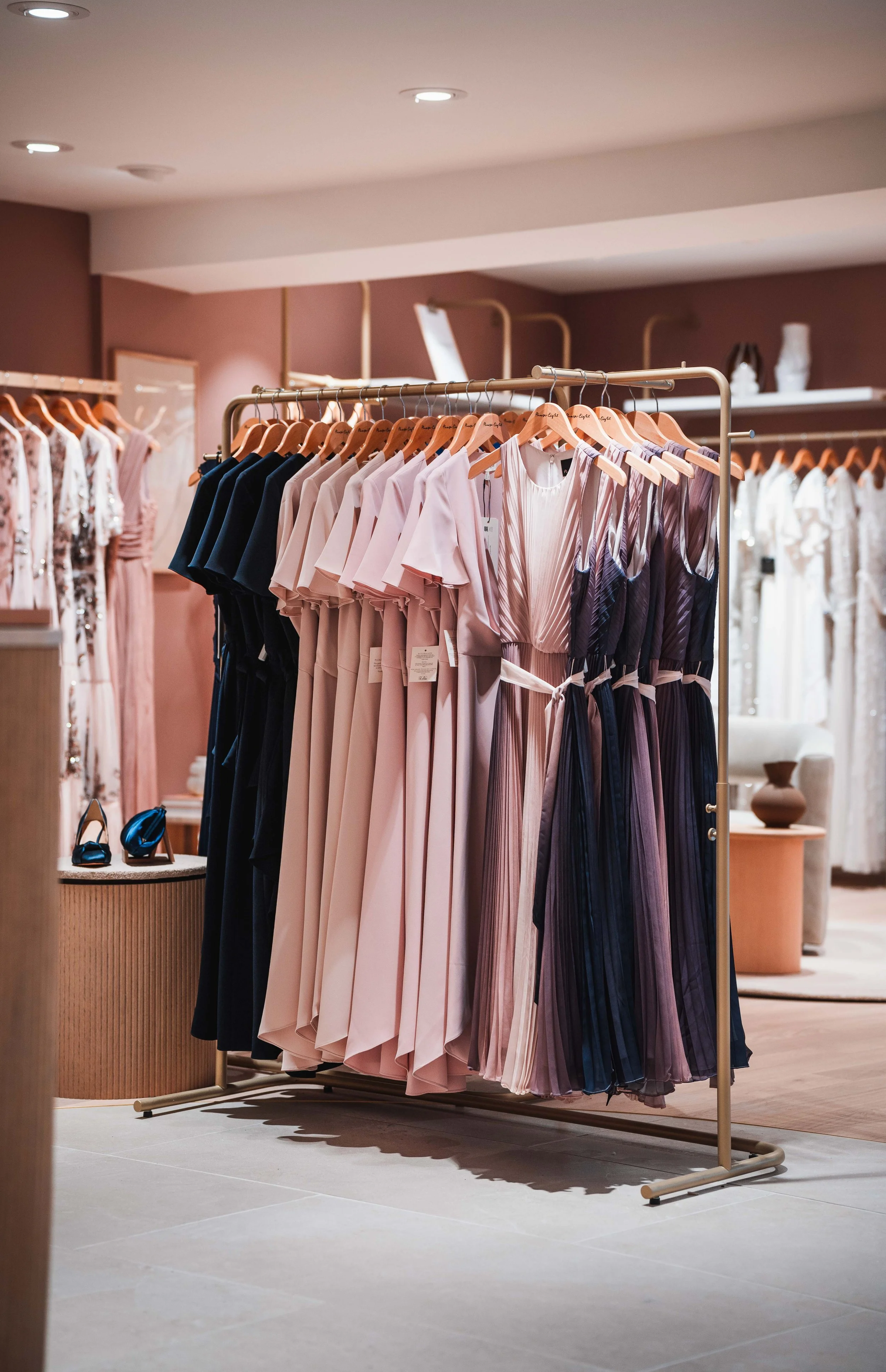 Clothing store display with dresses and jumpsuits on a rack, including pink, navy, and patterned items.