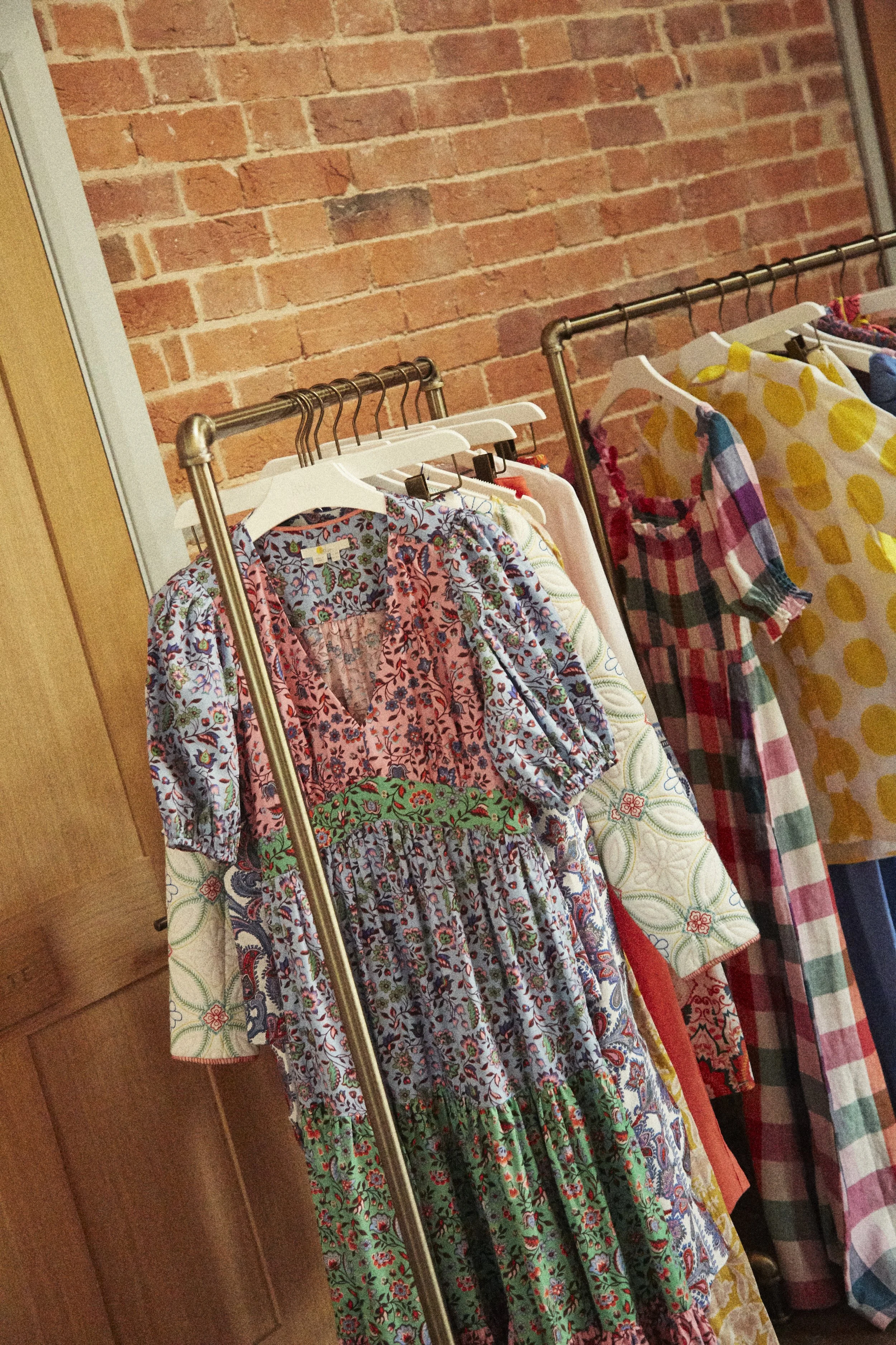 Clothing rack with various colorful dresses and shirts hanging against an exposed brick wall.
