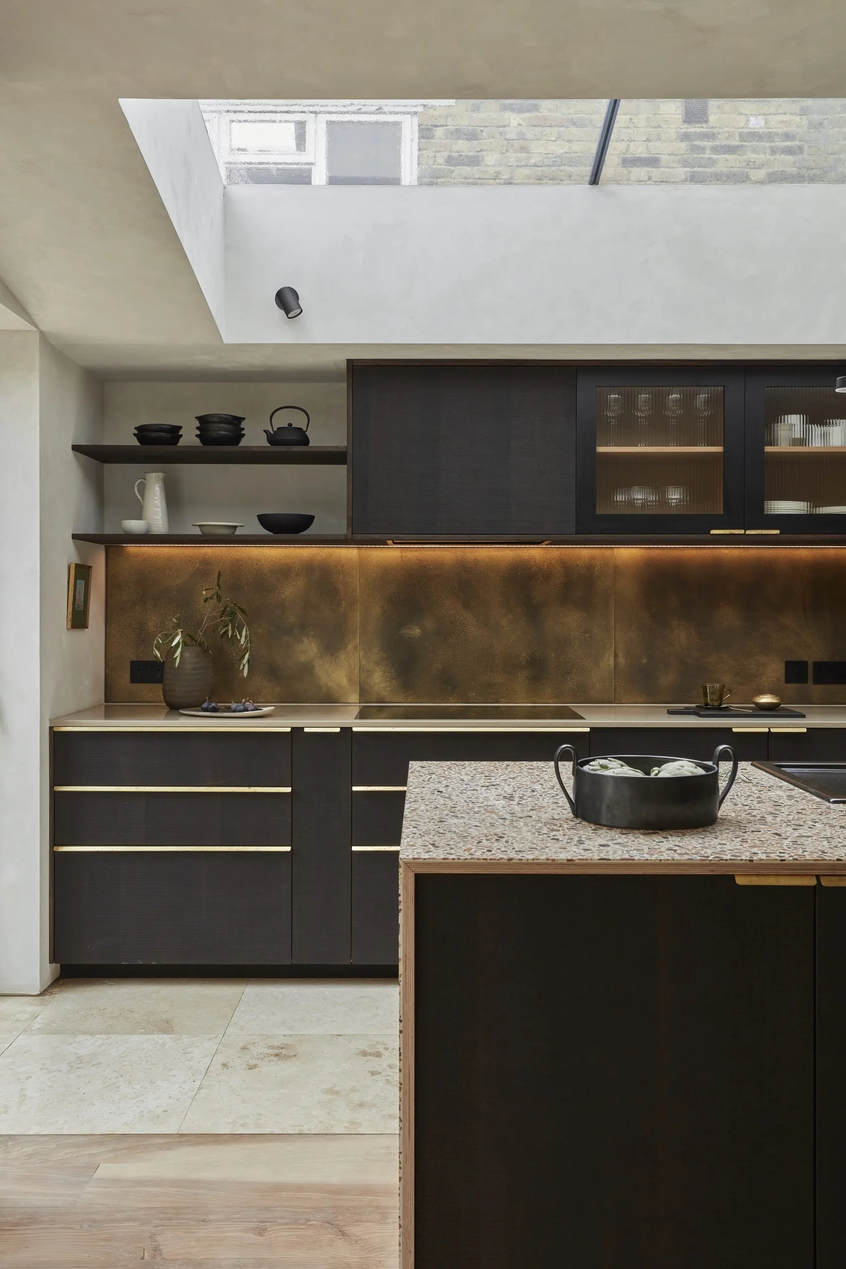 Modern kitchen with black cabinets, open shelves, a skylight, and a granite island with a black pot.