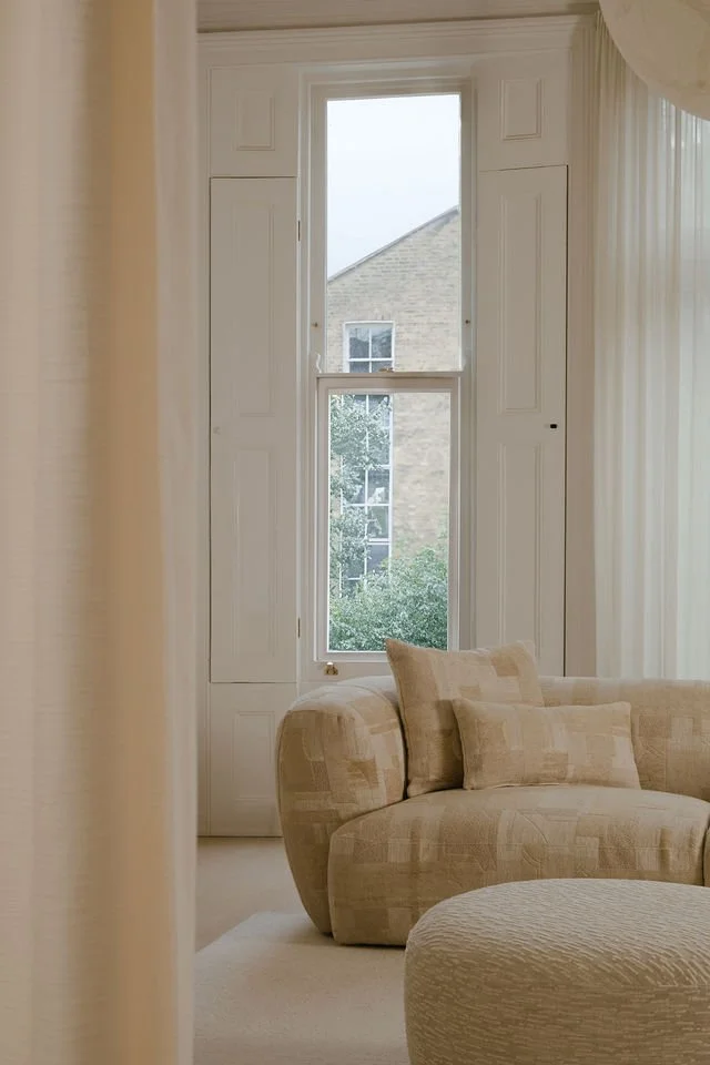 Living room with a large window, beige sectional sofa, and cream-colored curtains.