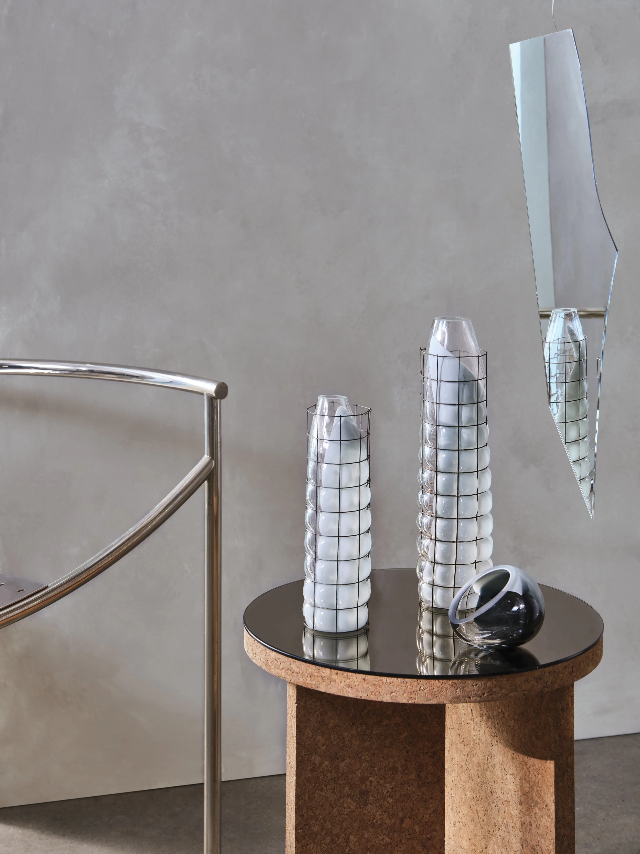 Decorative modern glass vases with bubble-like patterns and a black and white marble bowl on a small round table with a black glossy top, against a plain light-colored wall.