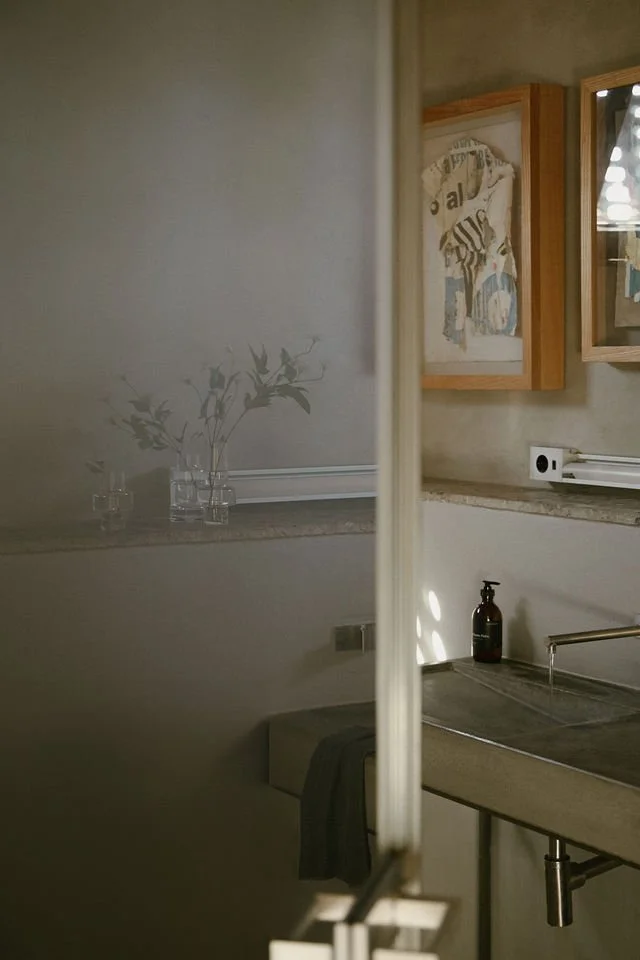 A partial view of a kitchen with a mirror reflecting a decorated shelf with glass vases and a framed art piece on the wall.