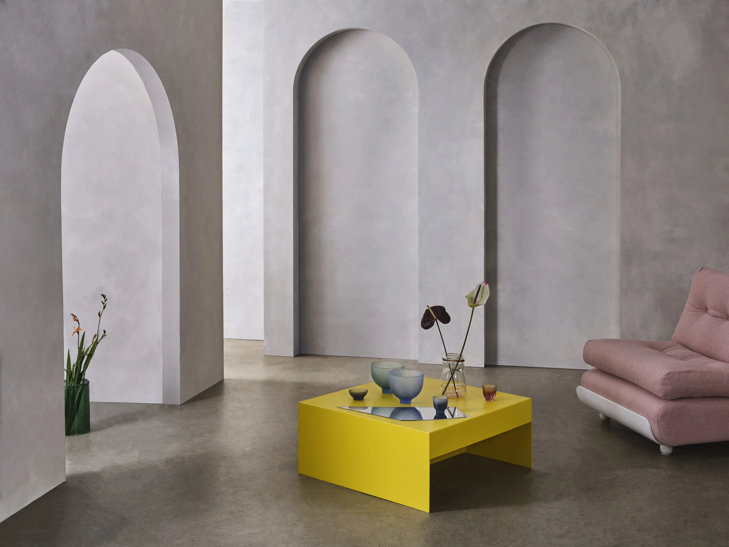 Modern interior room with arched doorways, a pink sofa, and a yellow table with decorative vases and plants.