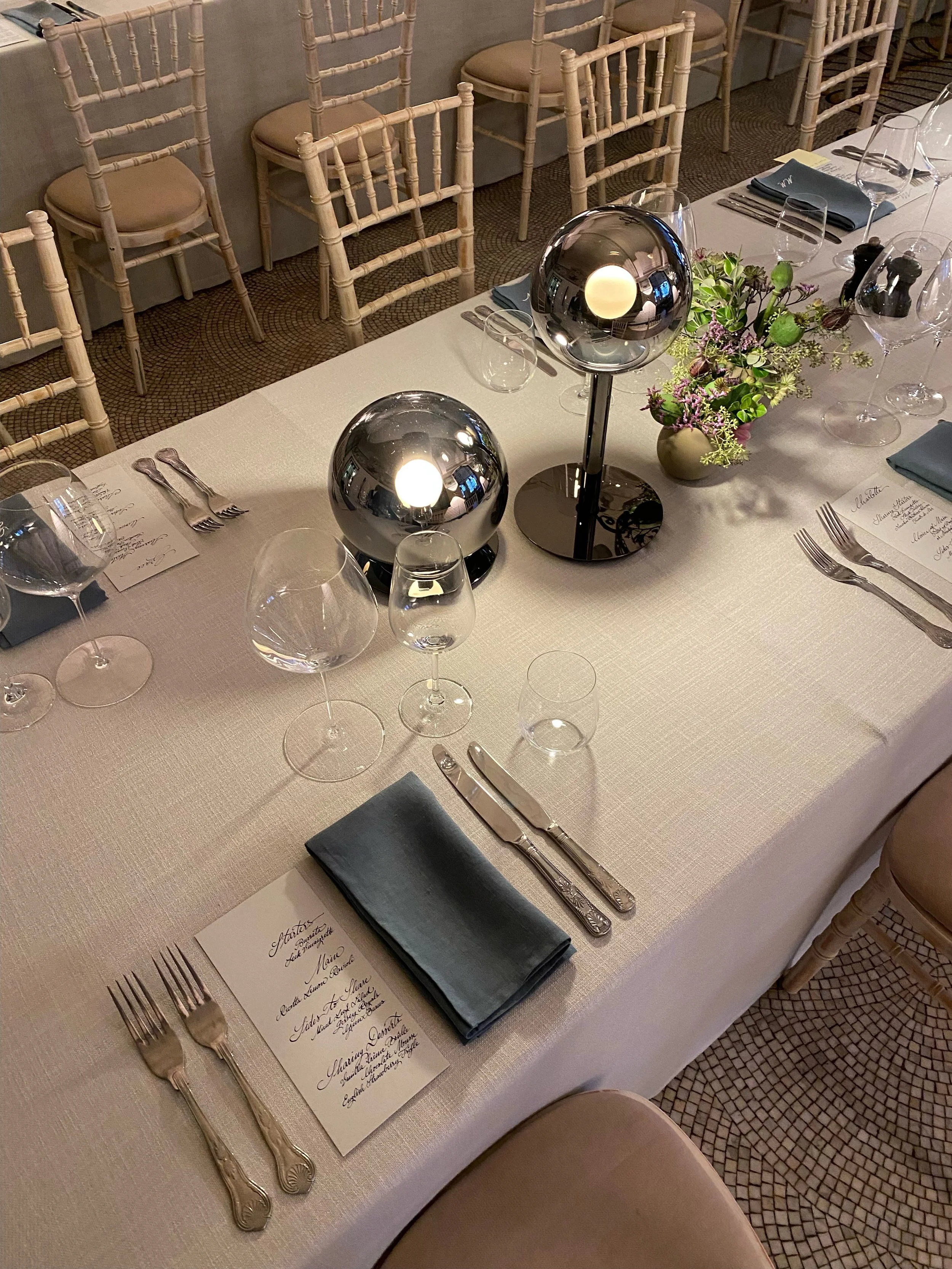 Elegant dining table set with silverware, glassware, black napkins, and a floral centerpiece, decorated with modern spherical lamps.