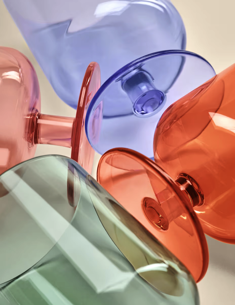 Close-up of colorful, translucent glass cups in green, pink, purple, orange, and blue stacked or laid overlapping each other.
