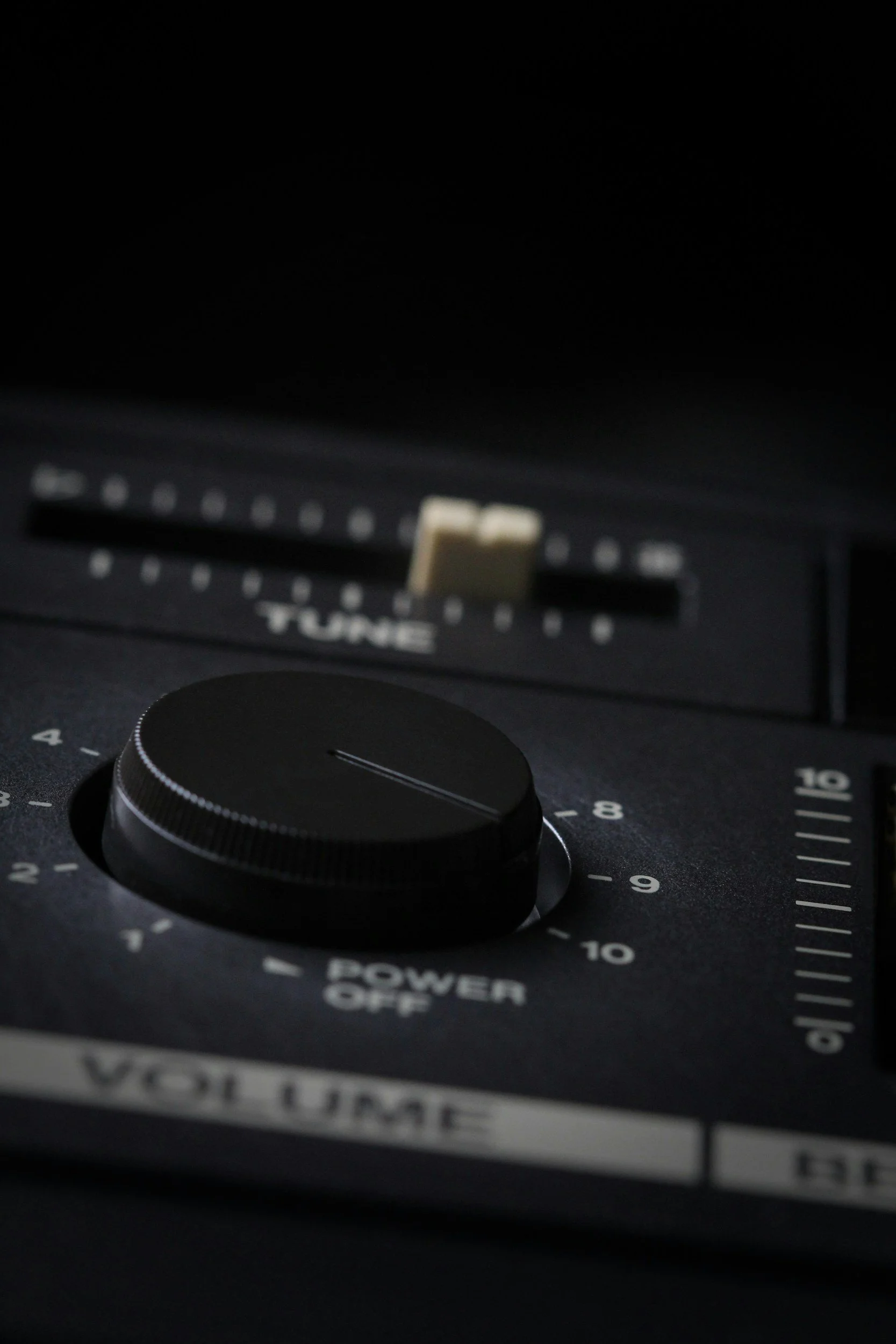 Close-up of a black vintage audio equipment with a large tuning knob, power switch, and tracking sliders, illuminated in low light.