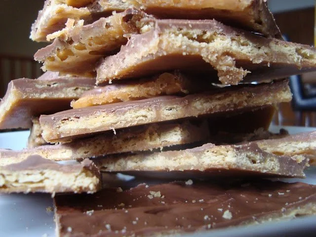 Stack of broken chocolate and biscuit-flavored layered candies or treats with a partially visible chocolate bar in the foreground.