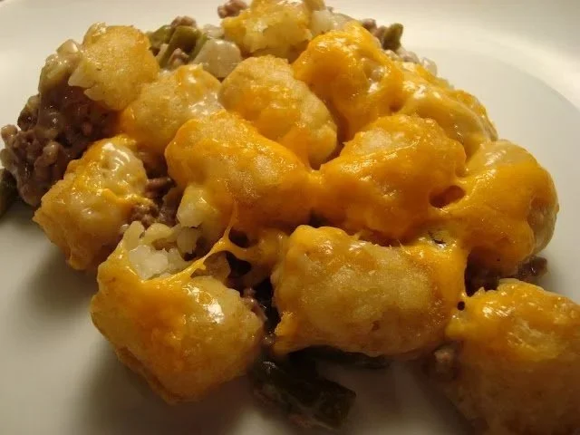 Baked cheesy tater tots served with ground beef and chopped onions on a white plate.