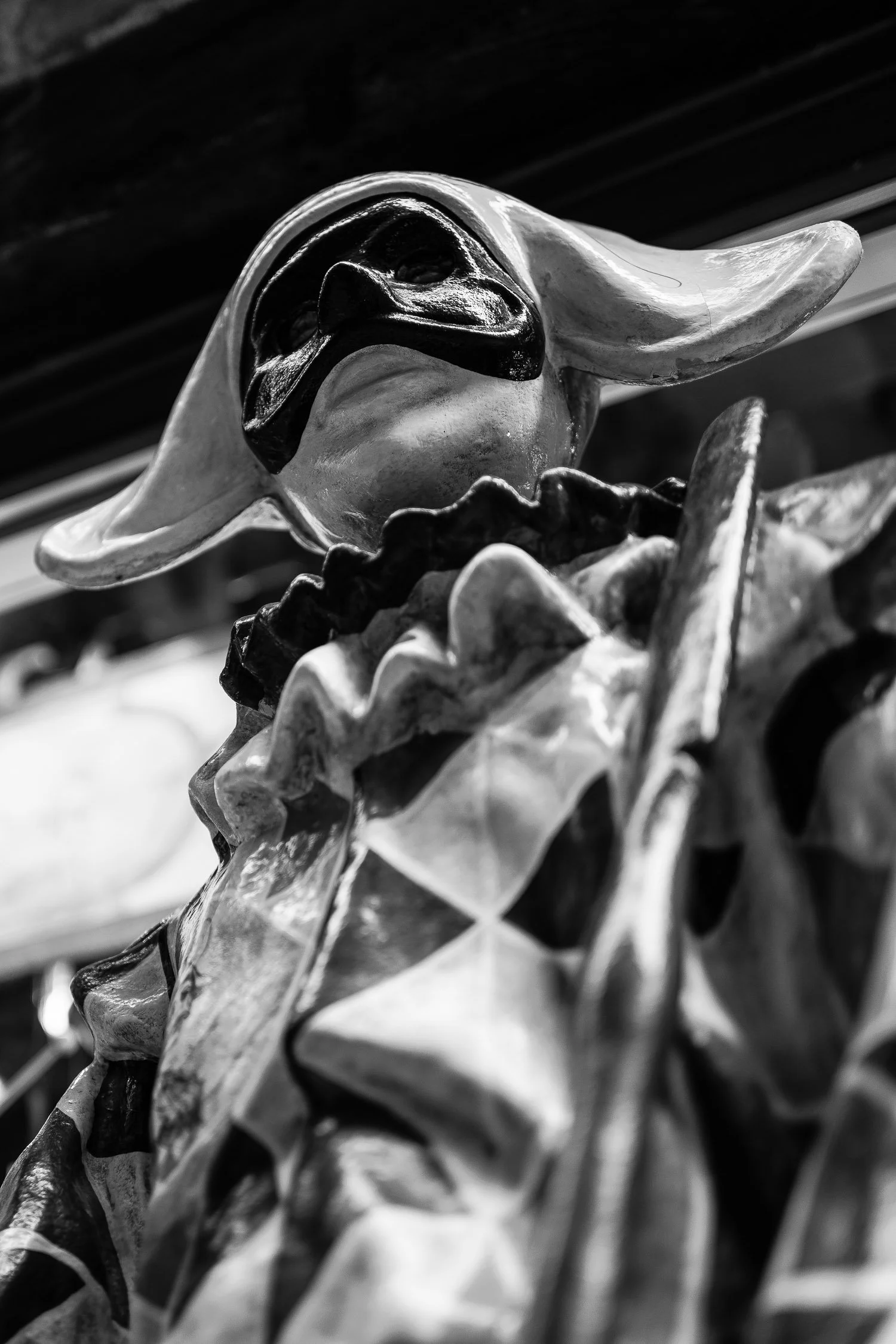 A close-up of a black and white statue depicting a masked figure in a ruffled costume, gazing upward with an elegant pose.