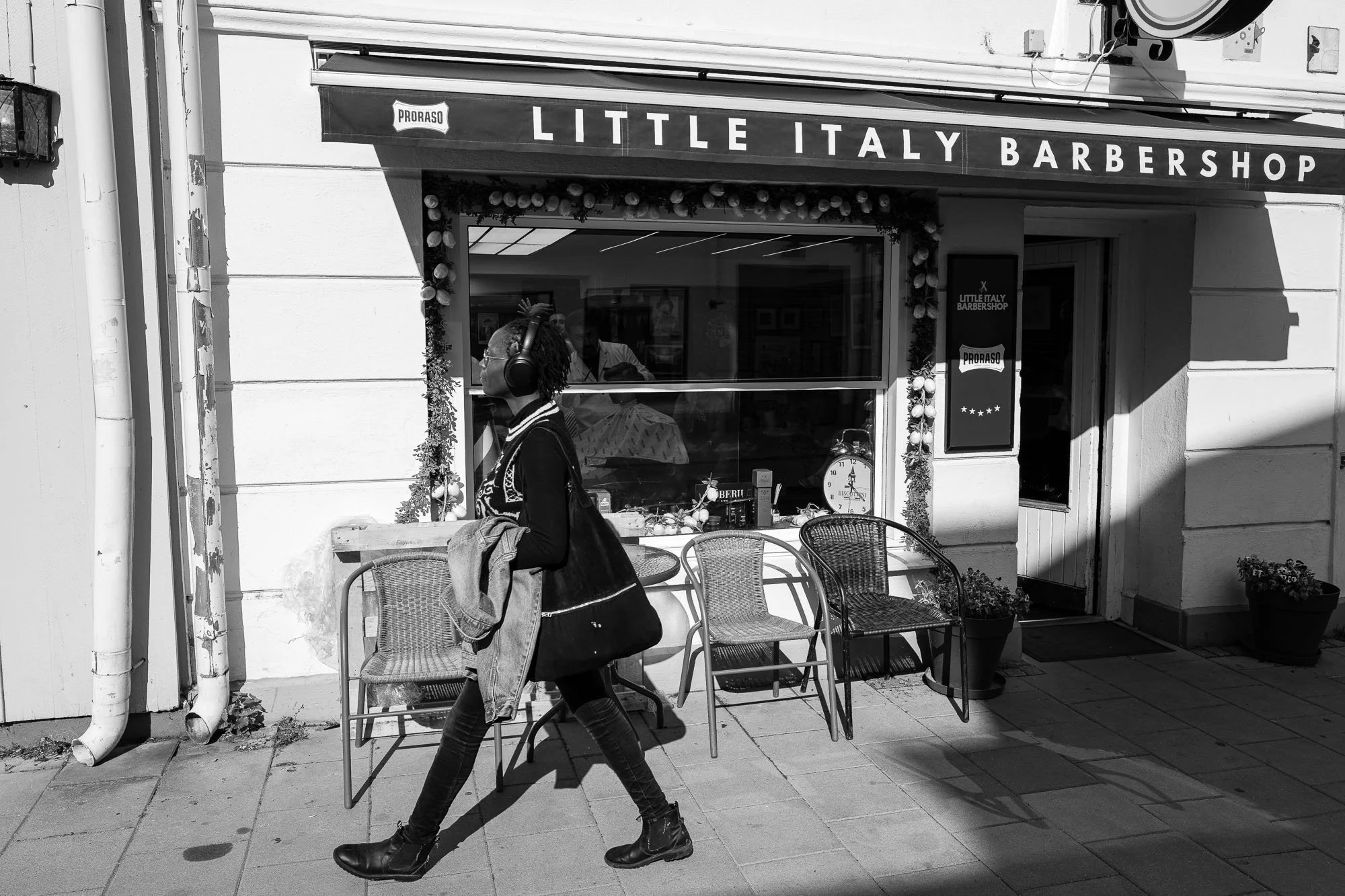 A person walks past the "Little Italy Barbershop," surrounded by elegant outdoor seating and festive decorations.