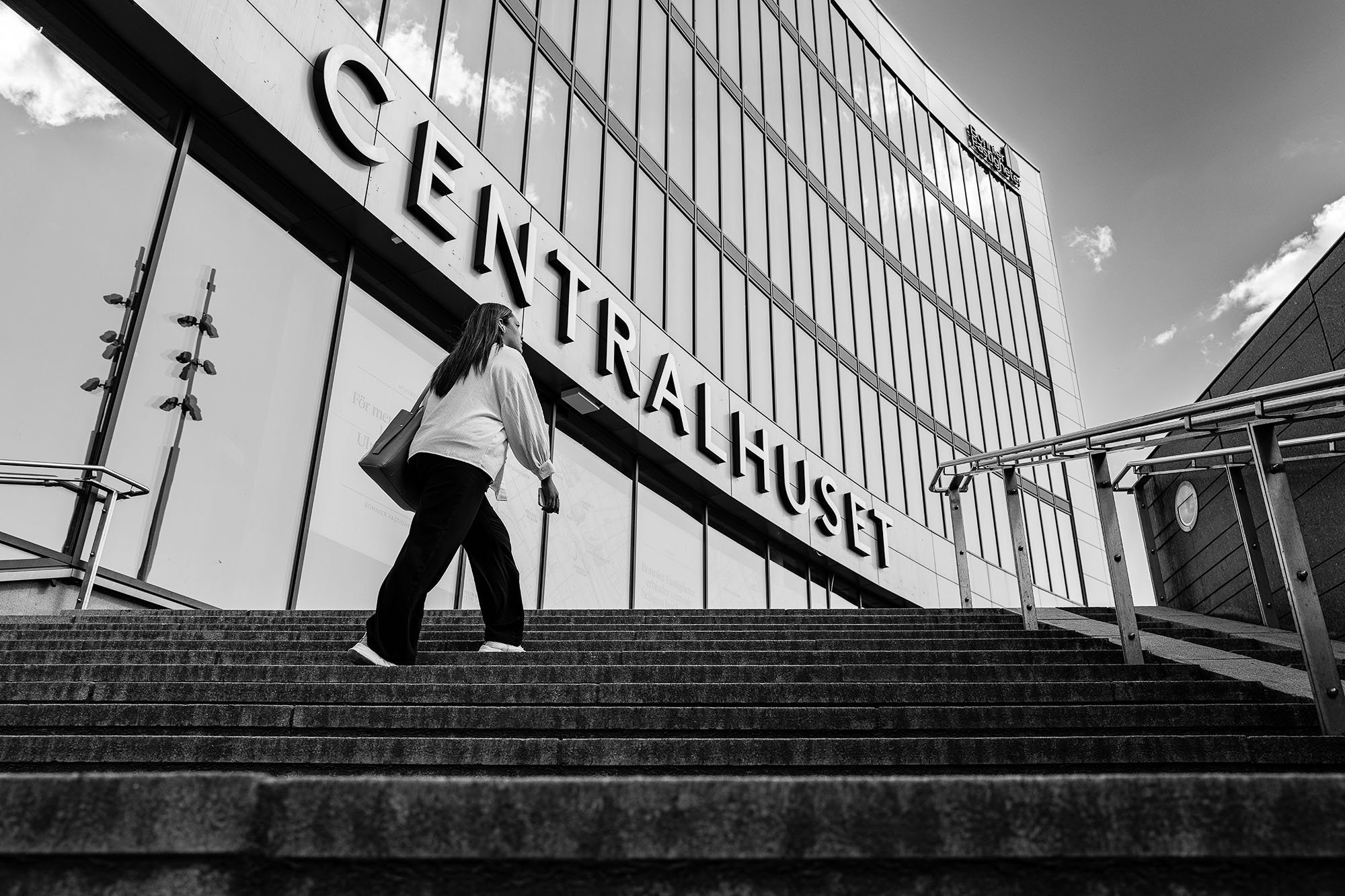 A person walks up the steps of a modern building with large glass windows and the sign "CENTRALHUSET" prominently displayed.