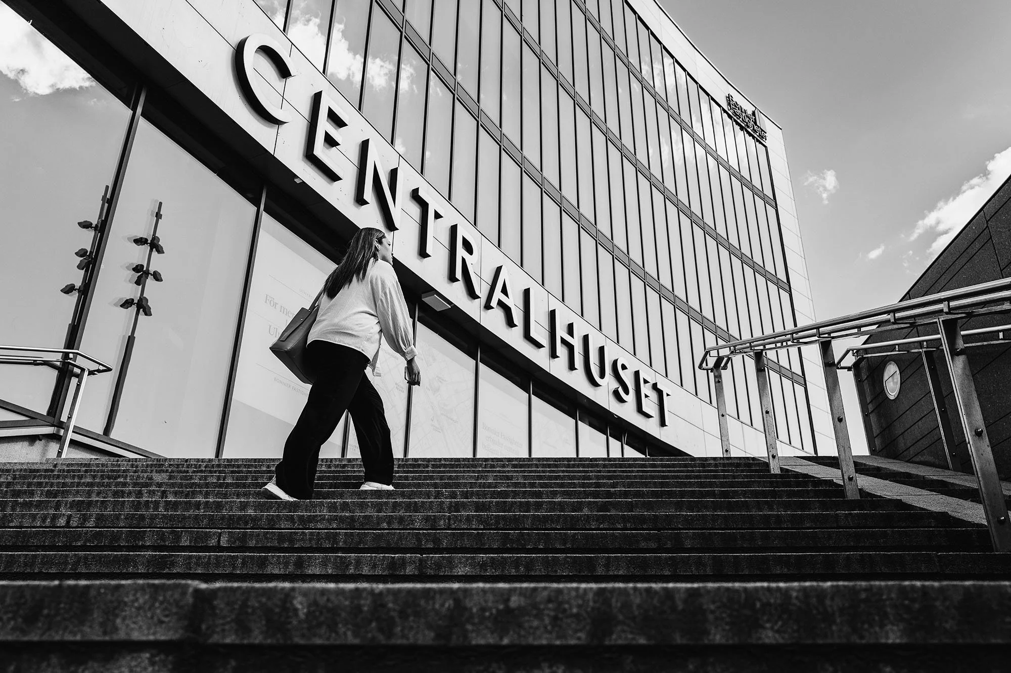 Black and white photo of a person walking up stairs towards a glass building with "Centralhuset" sign.