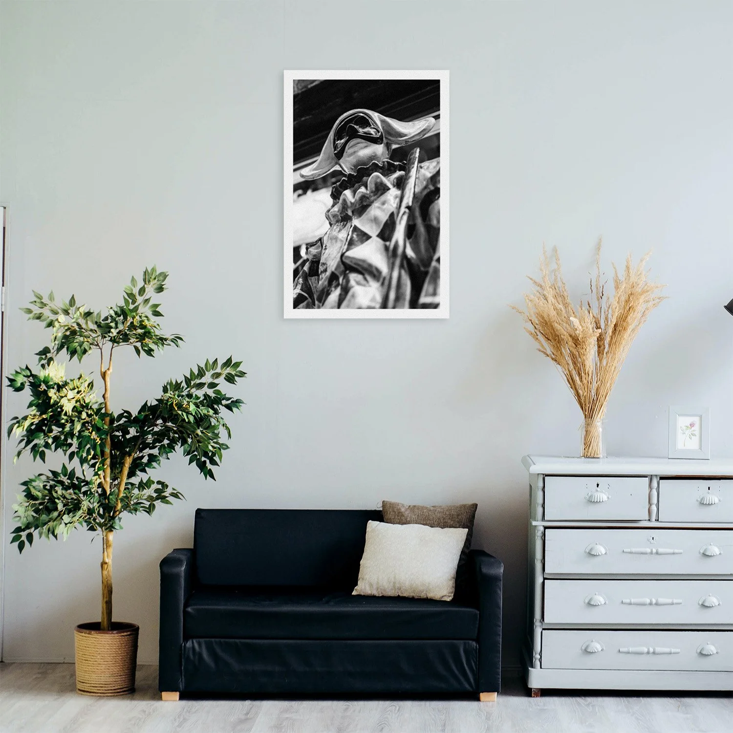 A modern living room featuring a black sofa, decorative plant, and a framed black-and-white artwork on the wall, adding elegance to the space.