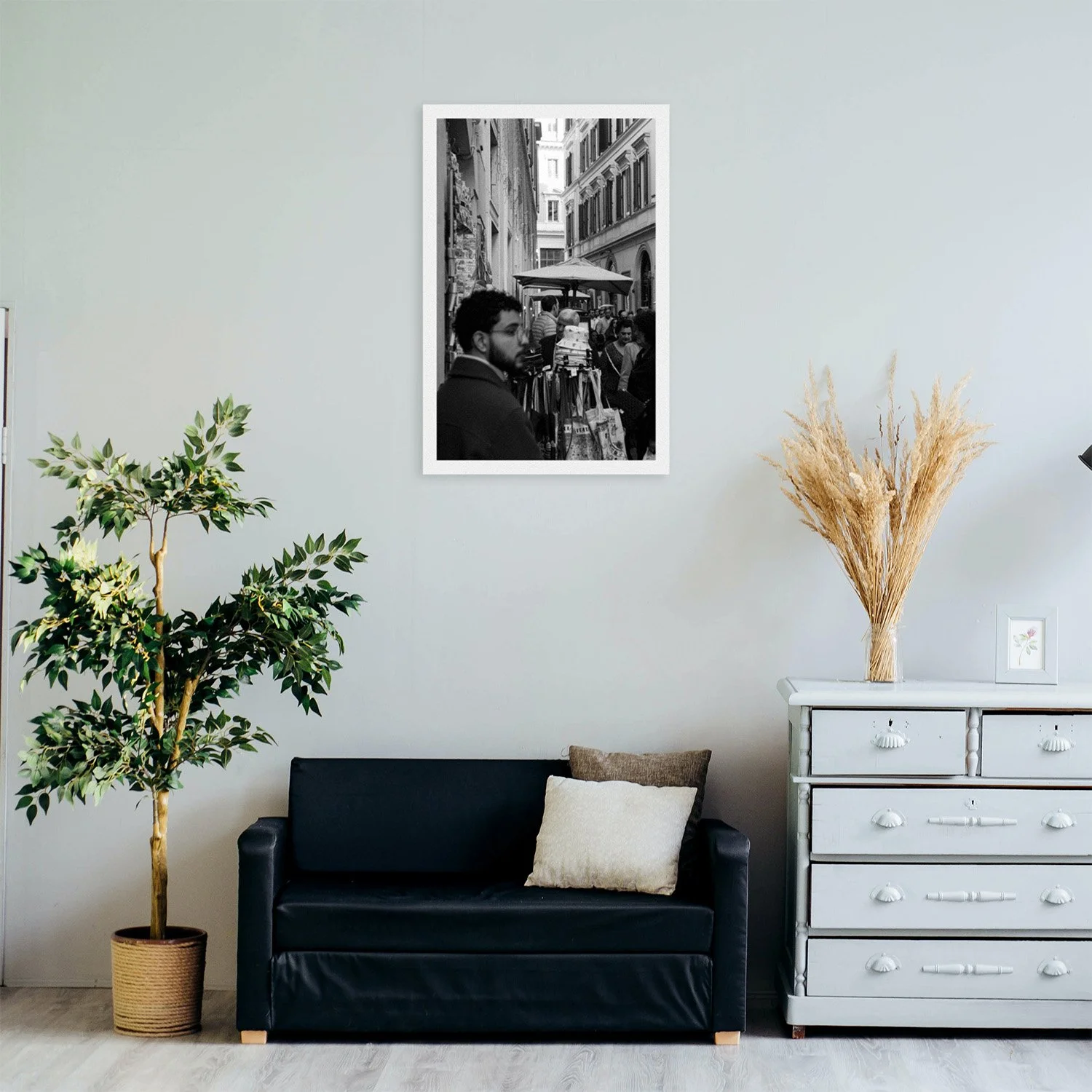 A cozy living room featuring a black couch, potted plant, and a light blue dresser, with a black and white photo on the wall.