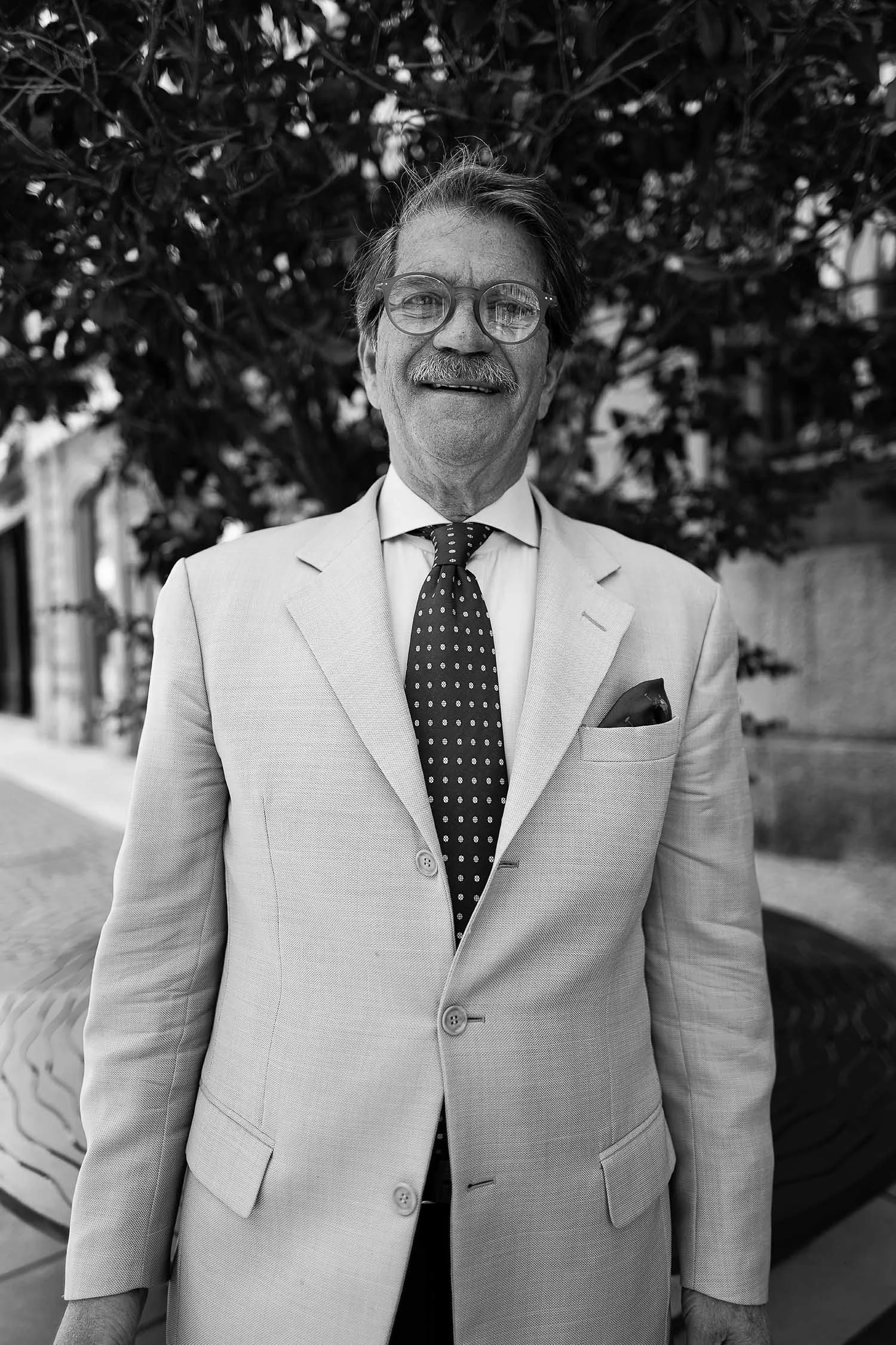 Gray-suited man wearing glasses and a patterned tie, outdoors.