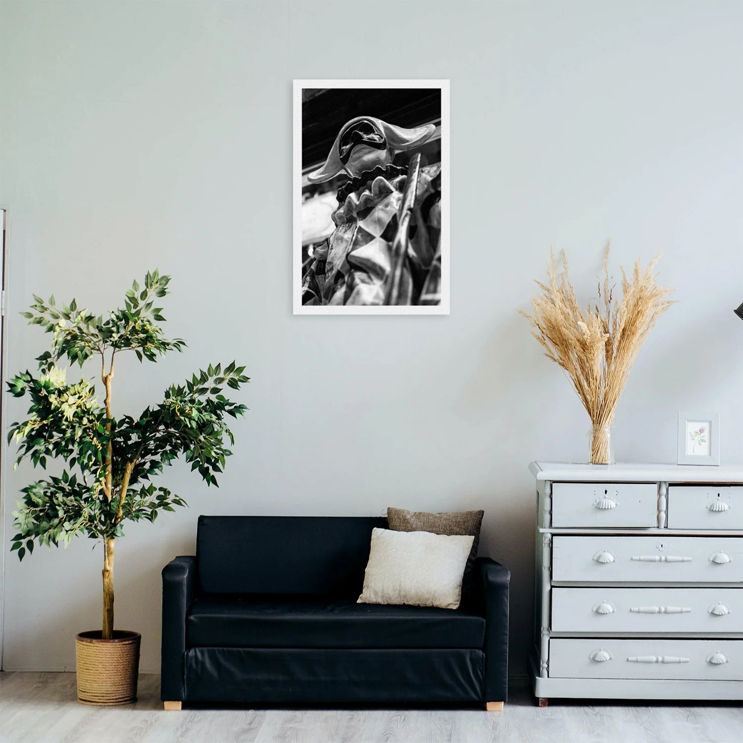 A modern living room featuring a black sofa, decorative plant, and a framed black-and-white artwork on the wall, adding elegance to the space.