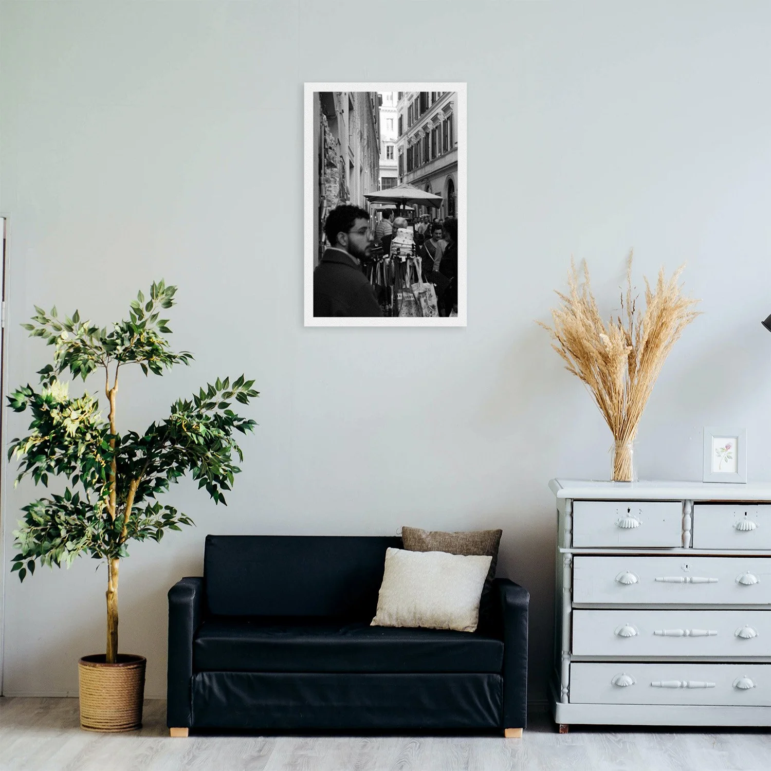 A cozy living room featuring a black couch, potted plant, and a light blue dresser, with a black and white photo on the wall.