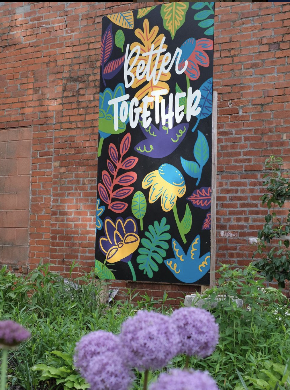 Photo of a hand painted mural with vibrant, artistic flowers and the saying "Better Together" written overtop the design.