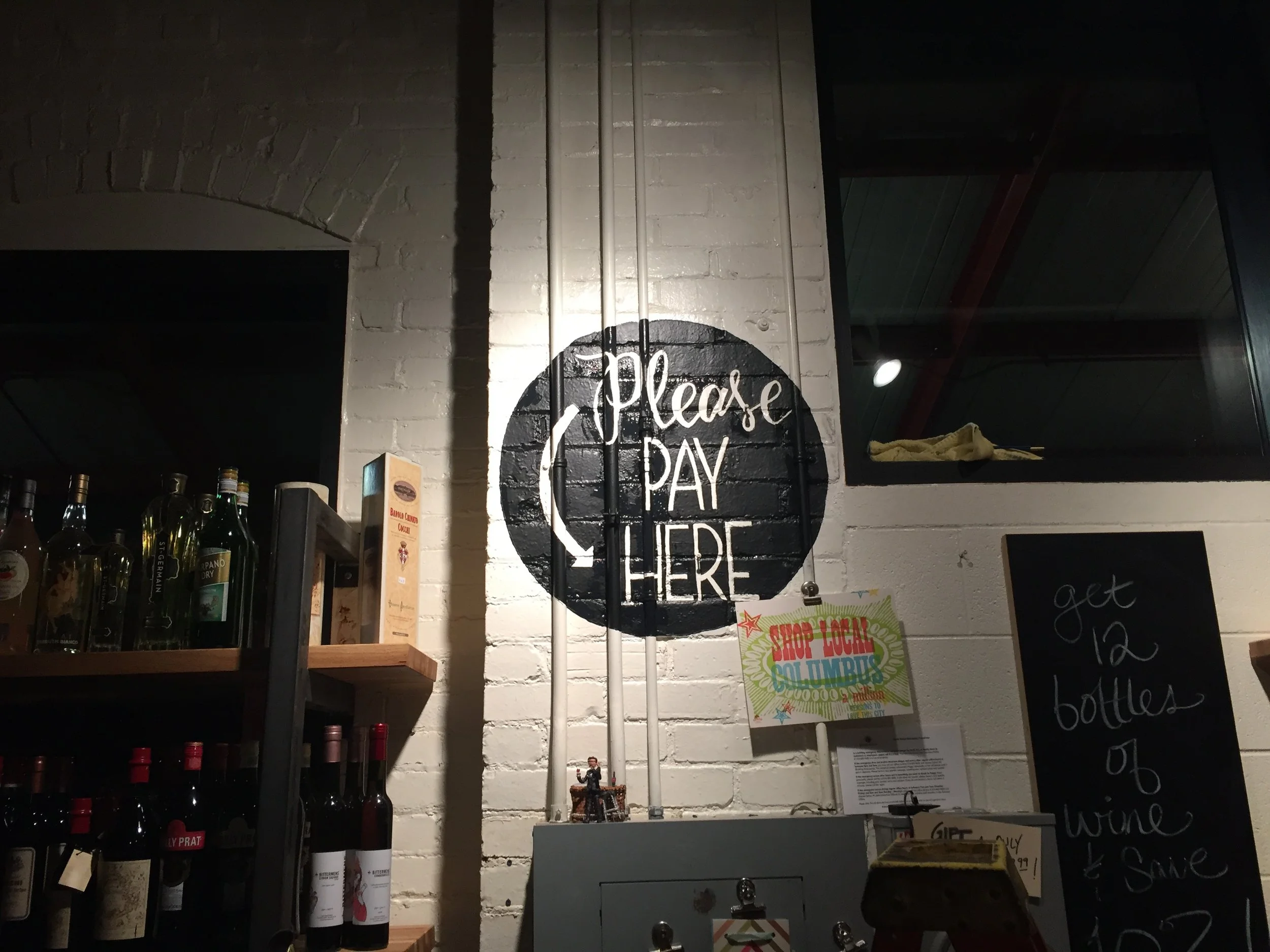 Hand Painted, hand lettered 'Please Pay Here" design overtop pipes on brick wall for The Barrel and Bottle.