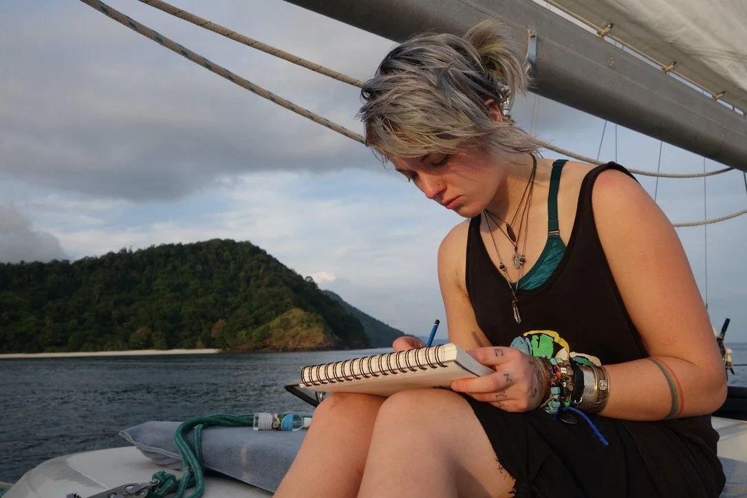 Katie Ford sits on a sailboat with a sketchbook in hand.