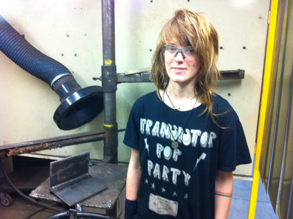 Katie stands in a welding booth in welding school