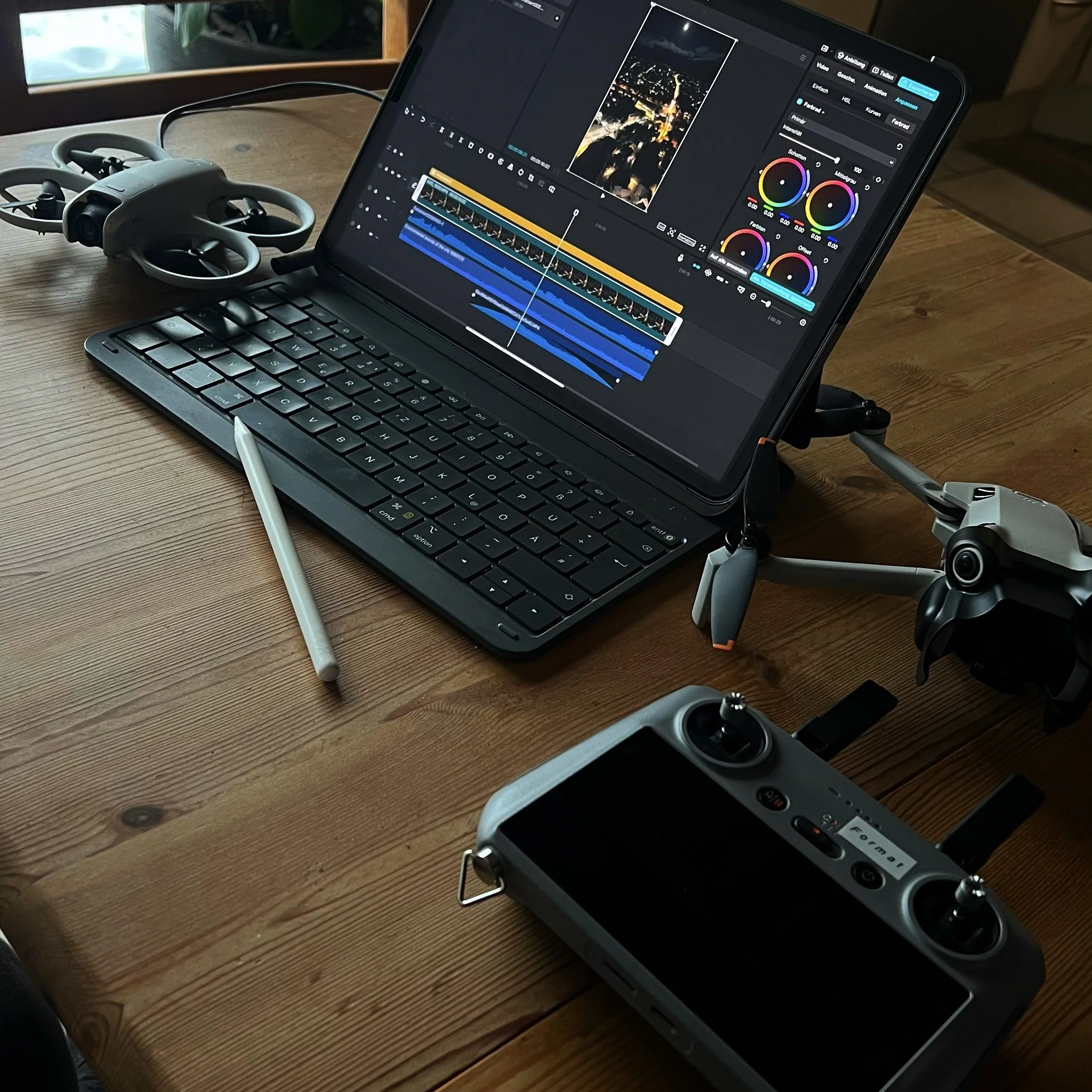Ein Laptop mit Video-Bearbeitungssoftware, eine Tastatur, ein digitaler Stift, eine Drohne und eine Fernsteuerung auf einem Holztisch.