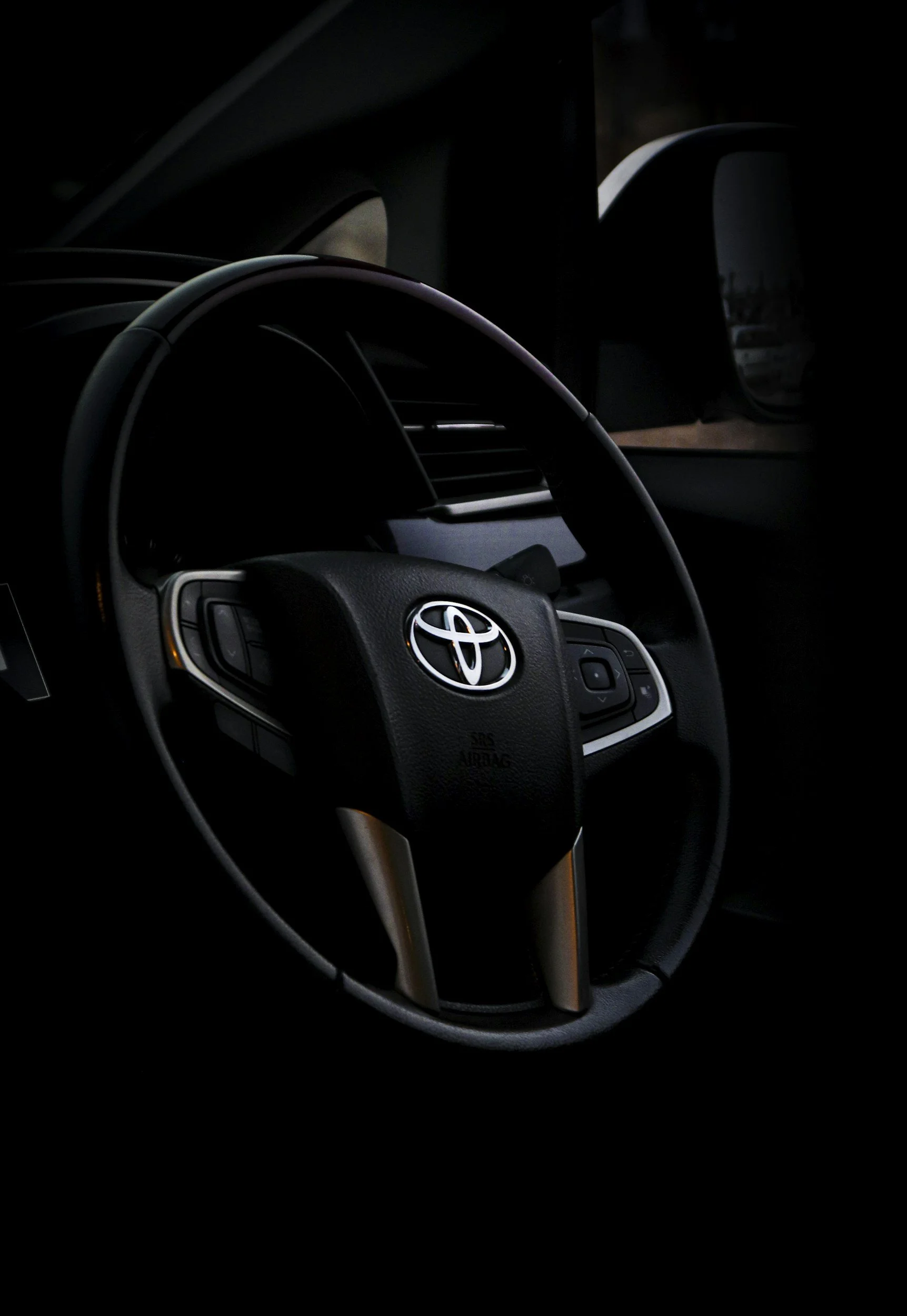 Close-up of a Toyota steering wheel inside a car, with a side mirror visible in the background.