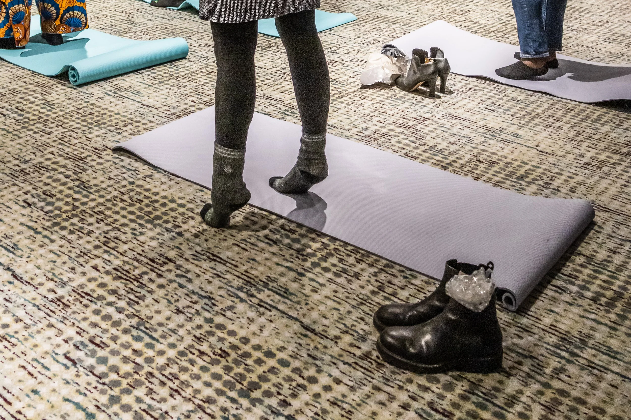People preparing for a yoga class, with yoga mats and shoes on the floor.