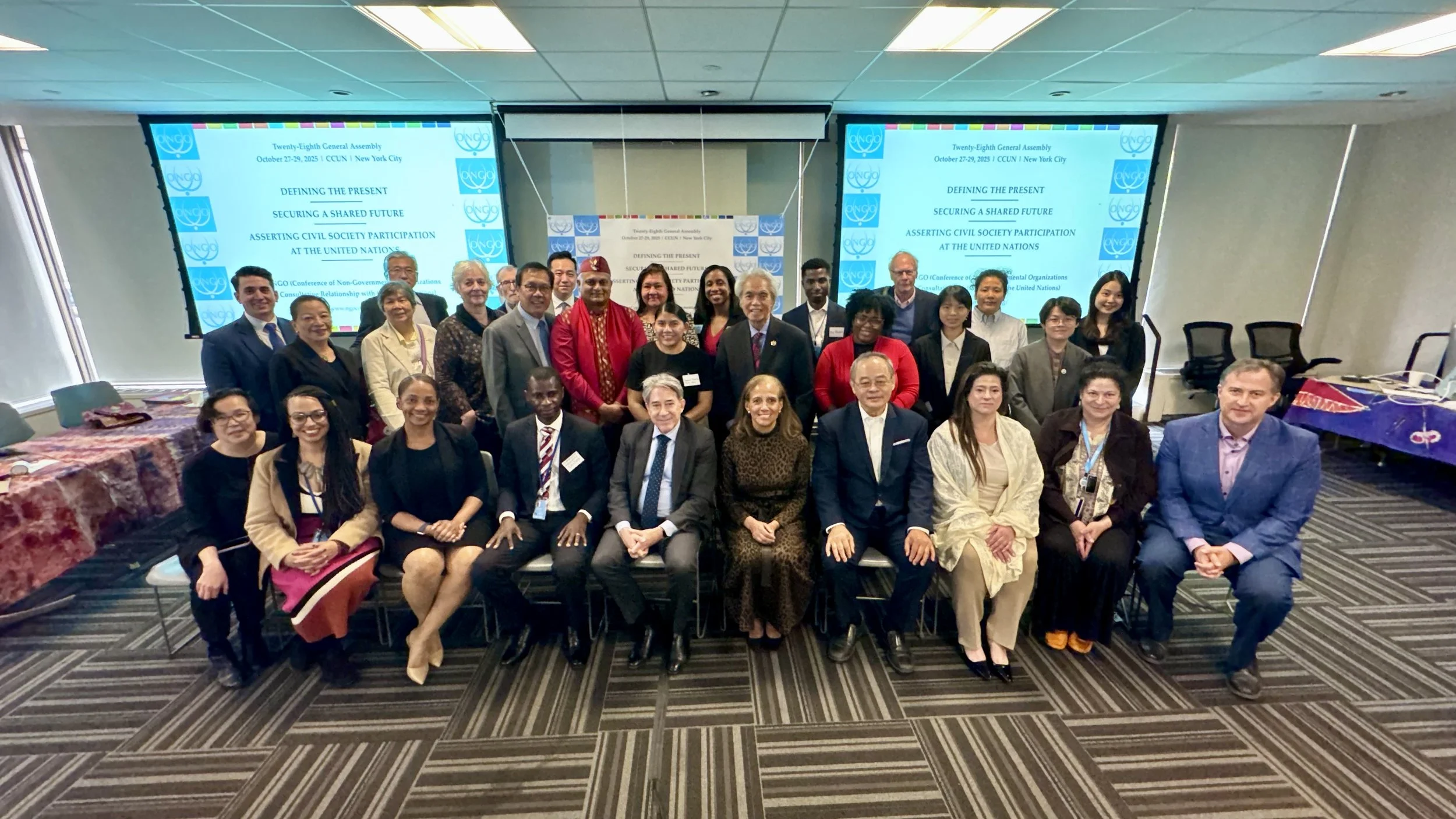 Group of diverse professionals posing for a photo at a conference on civil society participation at the United Nations, with presentation screens displaying the conference title in the background.