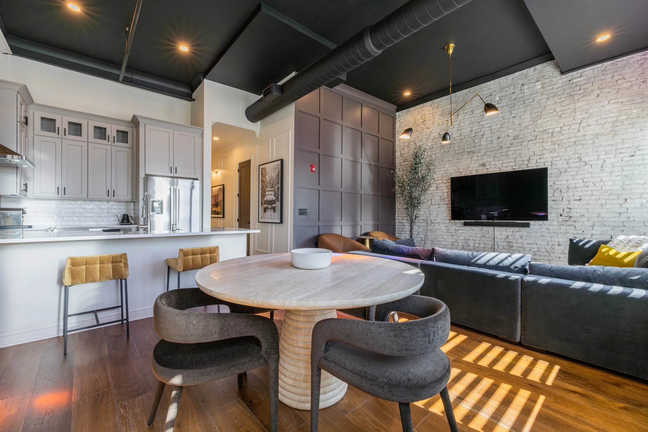 Open lounge and dining area with a round table, exposed ductwork, and an adjoining kitchen.
