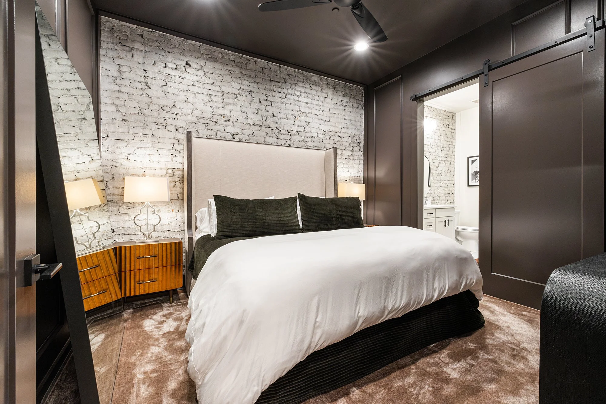 Bedroom with a white brick accent wall, white bedding, and a sliding bathroom door.