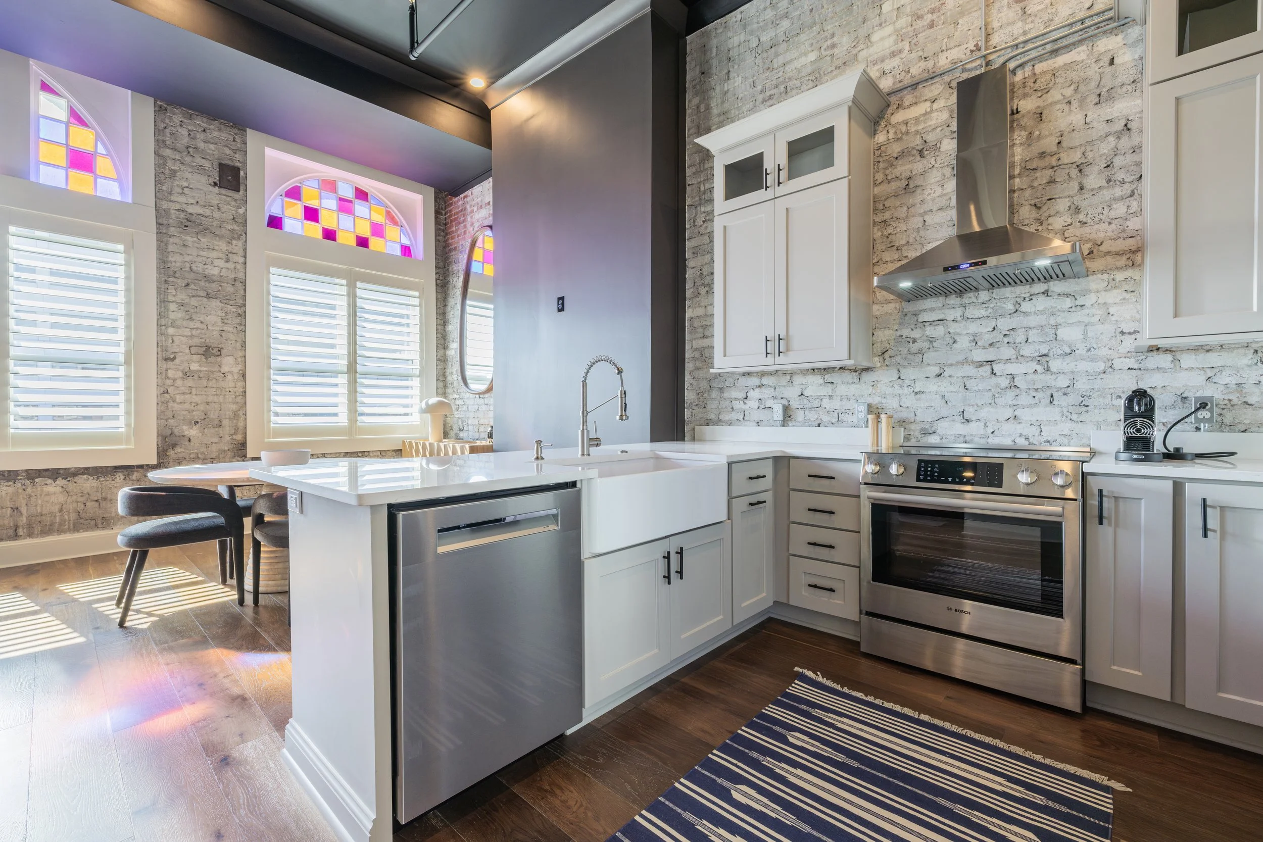 Kitchen with white cabinets, stainless steel appliances, exposed brick, and stained glass windows.