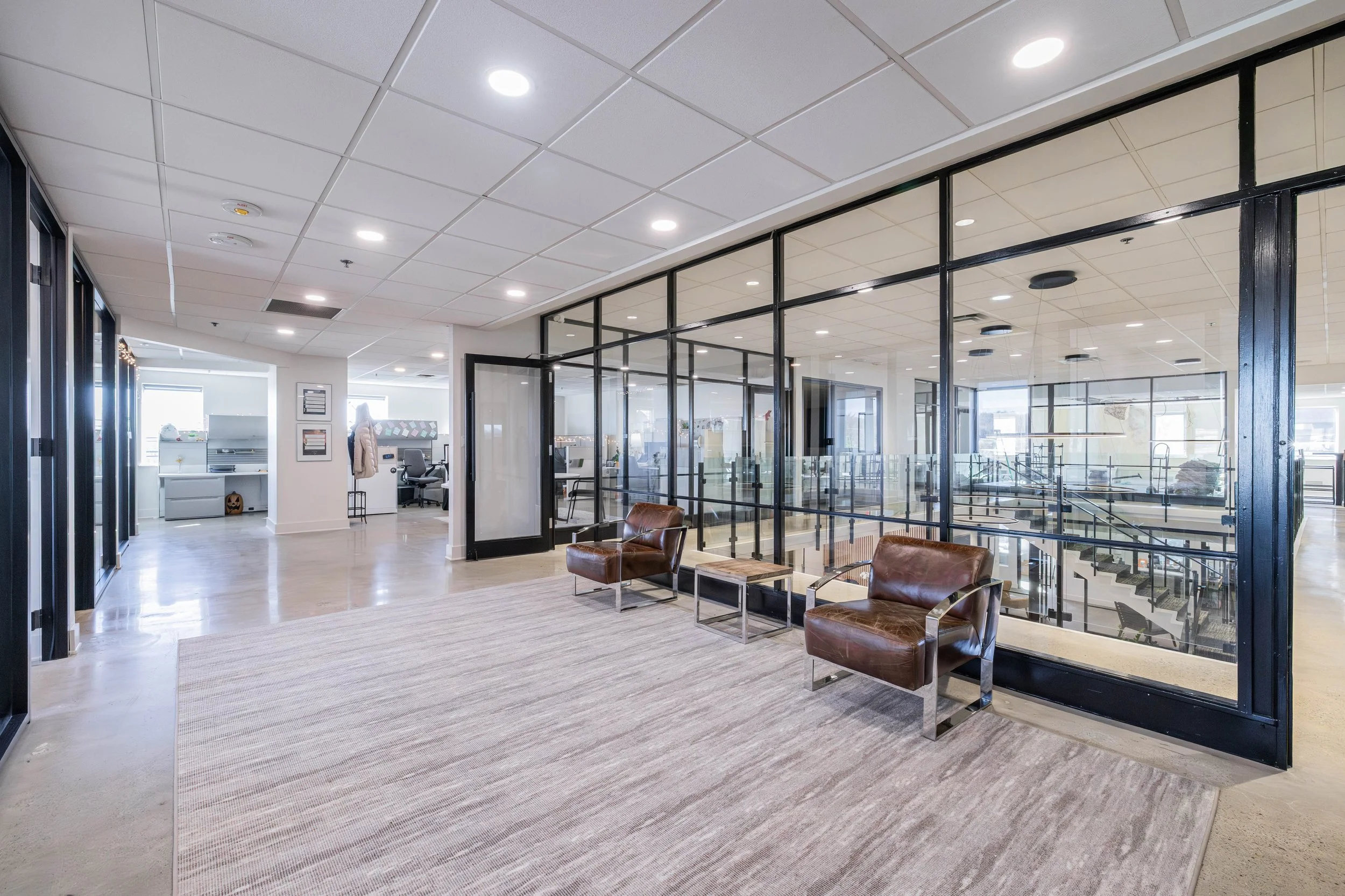 Interior view of an office space with modern furniture, large glass walls, and ceiling lights.