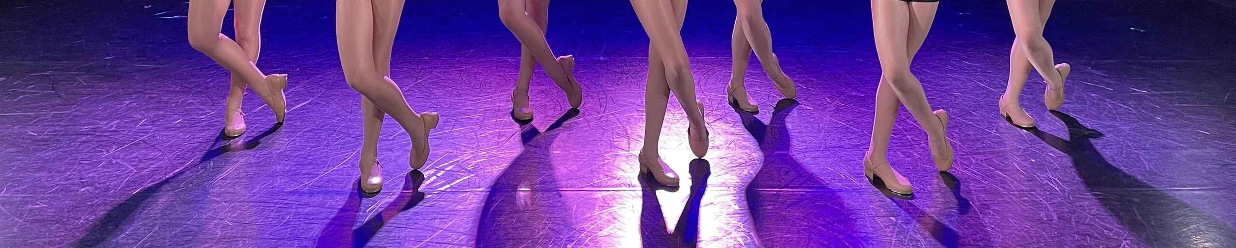 Group of dancers in pink costumes performing on stage with purple lighting.
