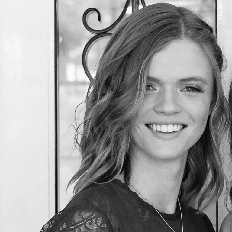 Black and white photo of a smiling woman with wavy hair and a lacy top.