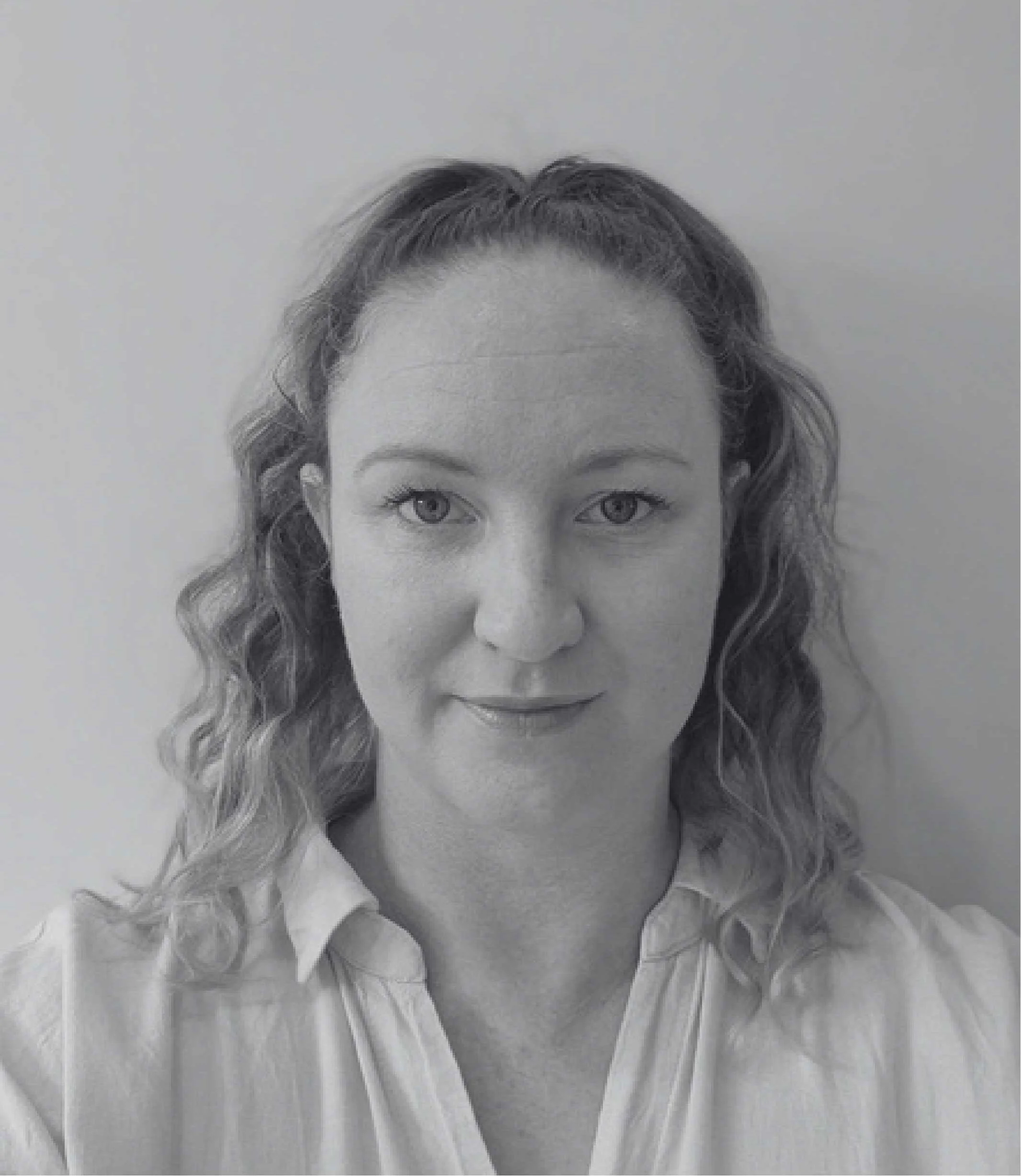 Close-up black-and-white photo of a woman's face with light-colored wavy hair wearing a white shirt or blouse.