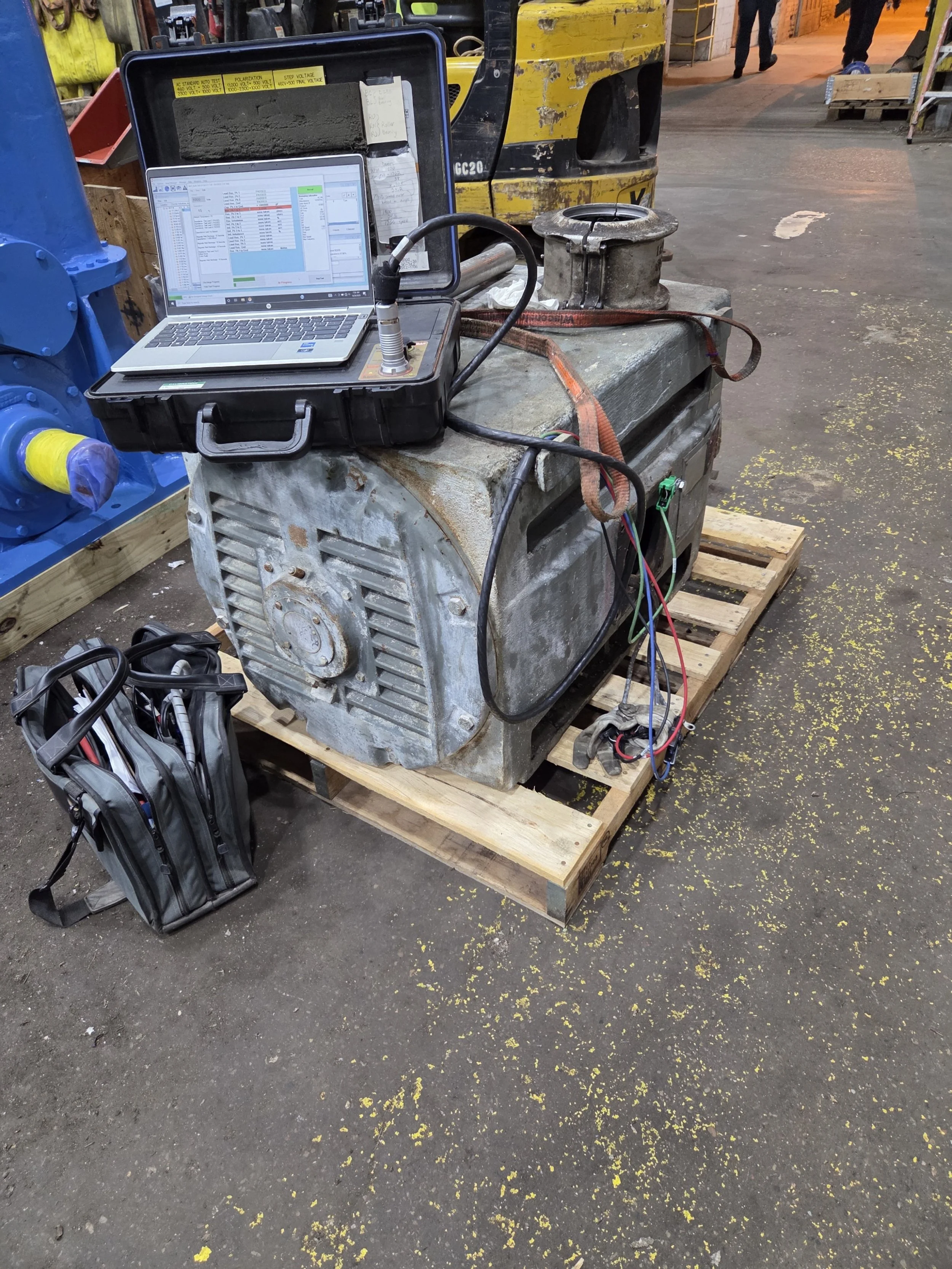 Industrial equipment with a laptop and testing device set up on a wooden pallet in a warehouse or factory. Offline motor testing. Baseline motor test. 2300 volt AC.