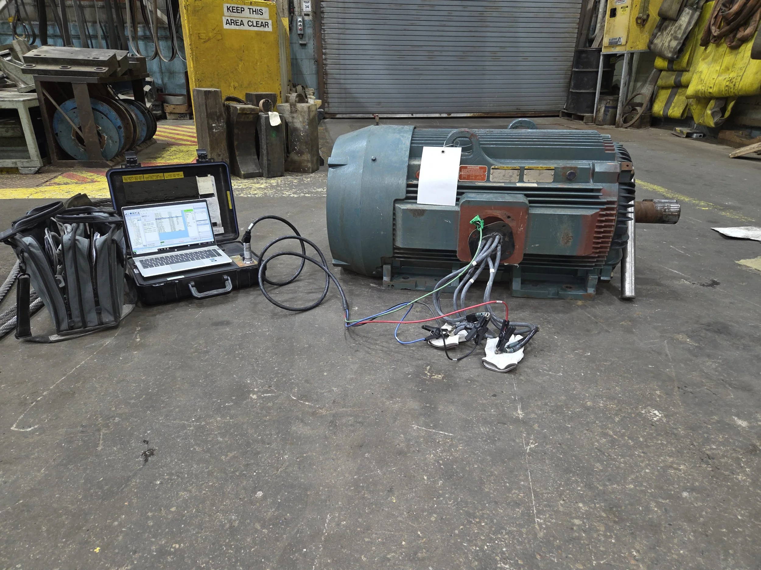 Large electric motor connected to a laptop and testing equipment on concrete floor in industrial workshop. Offline motor testing. Predictive motor testing. Baseline testing.