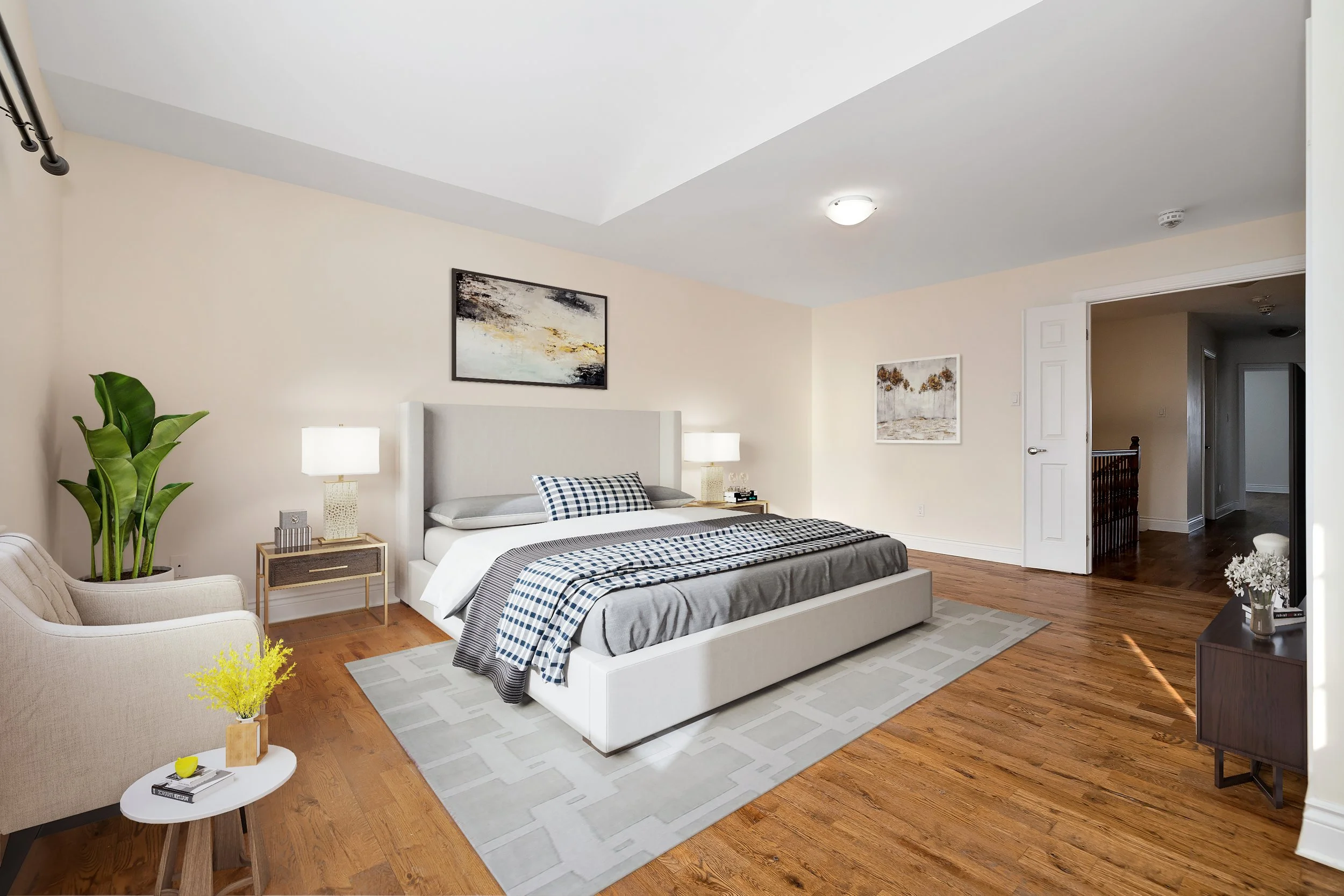 A modern bedroom with a large bed, two lamps, a beige armchair, a small white side table with a yellow plant, and artwork on the walls. Hardwood floor and a light-colored area rug.