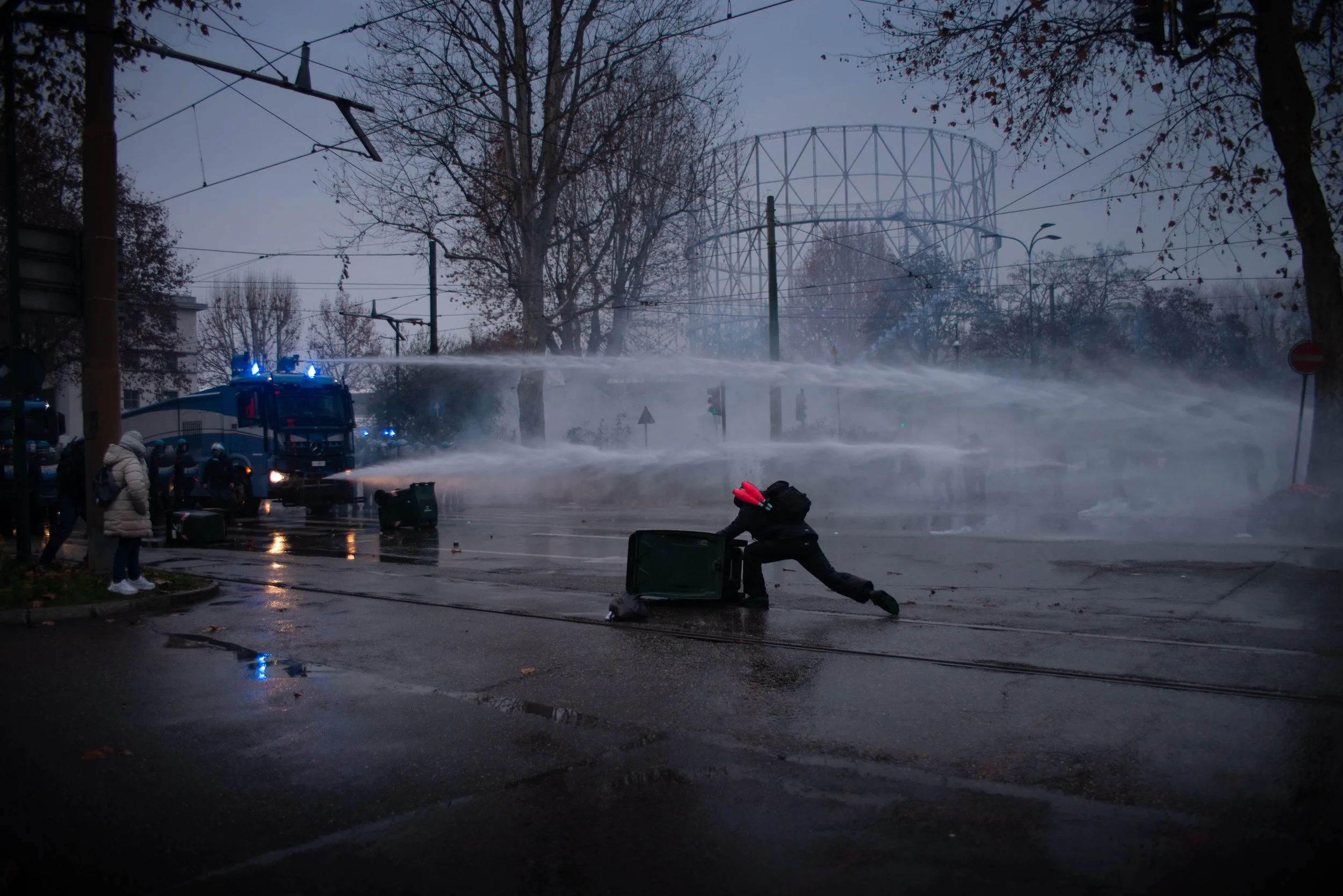 Turin, Italy – December 20, 2025: Riot police advance with shields raised while demonstrators push back with flags and poles amid water cannon blasts near the former Askatasuna social center.