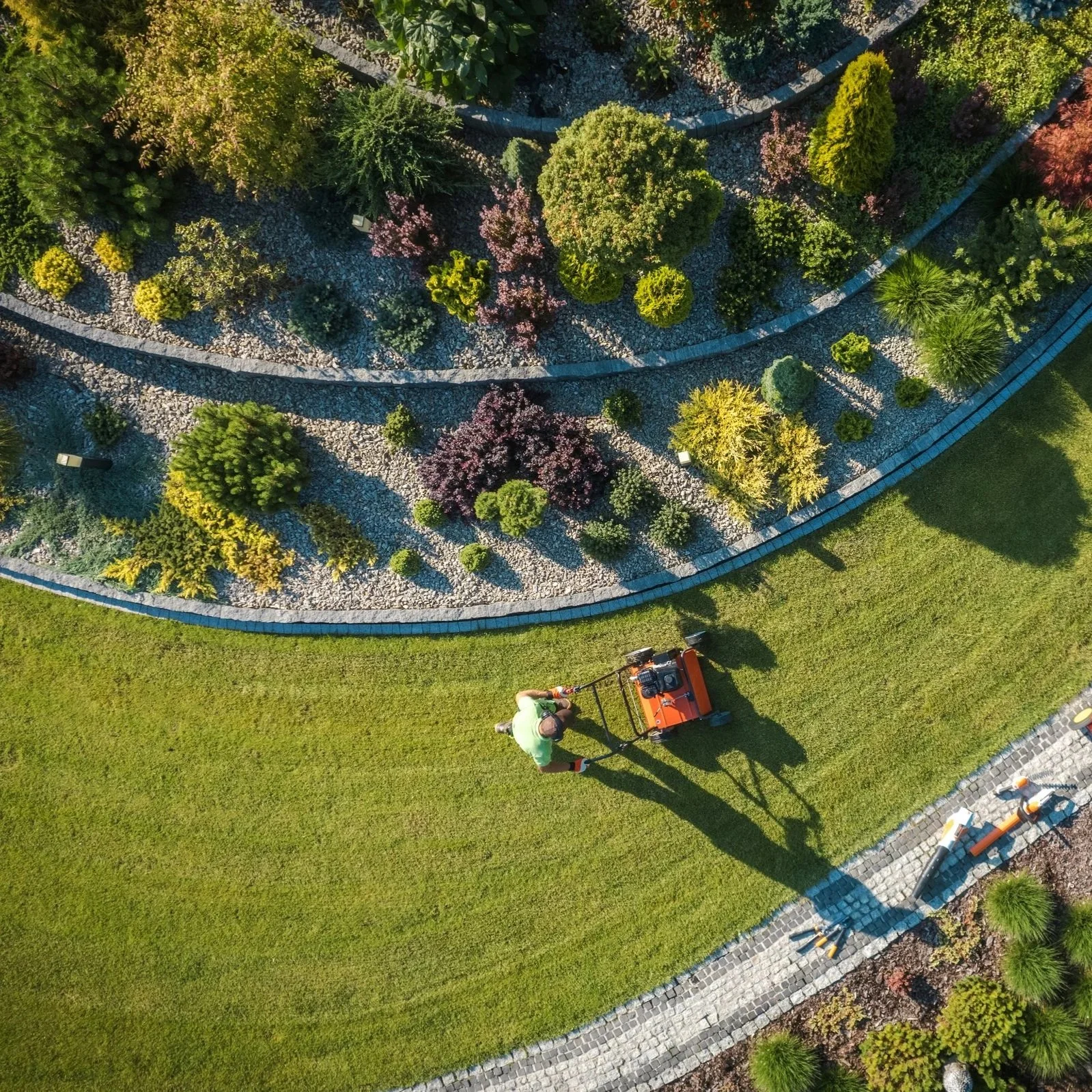 A person performing core aeration service in a lawn with curved stone pathways and colorful trees.
