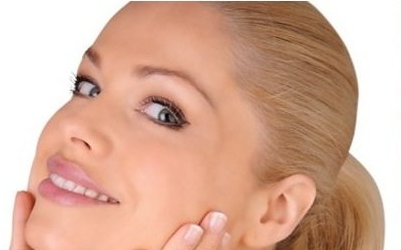 Close-up of a smiling woman with blonde hair, touching her cheek.