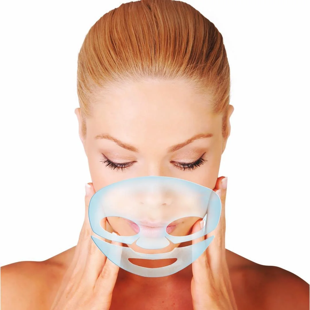 Woman with blonde hair using a clear facial sheet mask on her face against a white background.