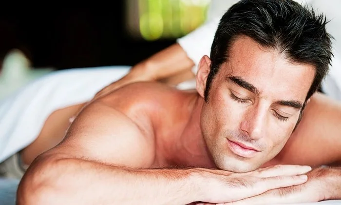 A man receiving a massage, lying face down with eyes closed, in a relaxing environment.