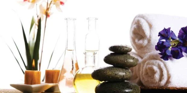 Spa setting with rolled white towels, purple flowers, candles, and stones for relaxation.